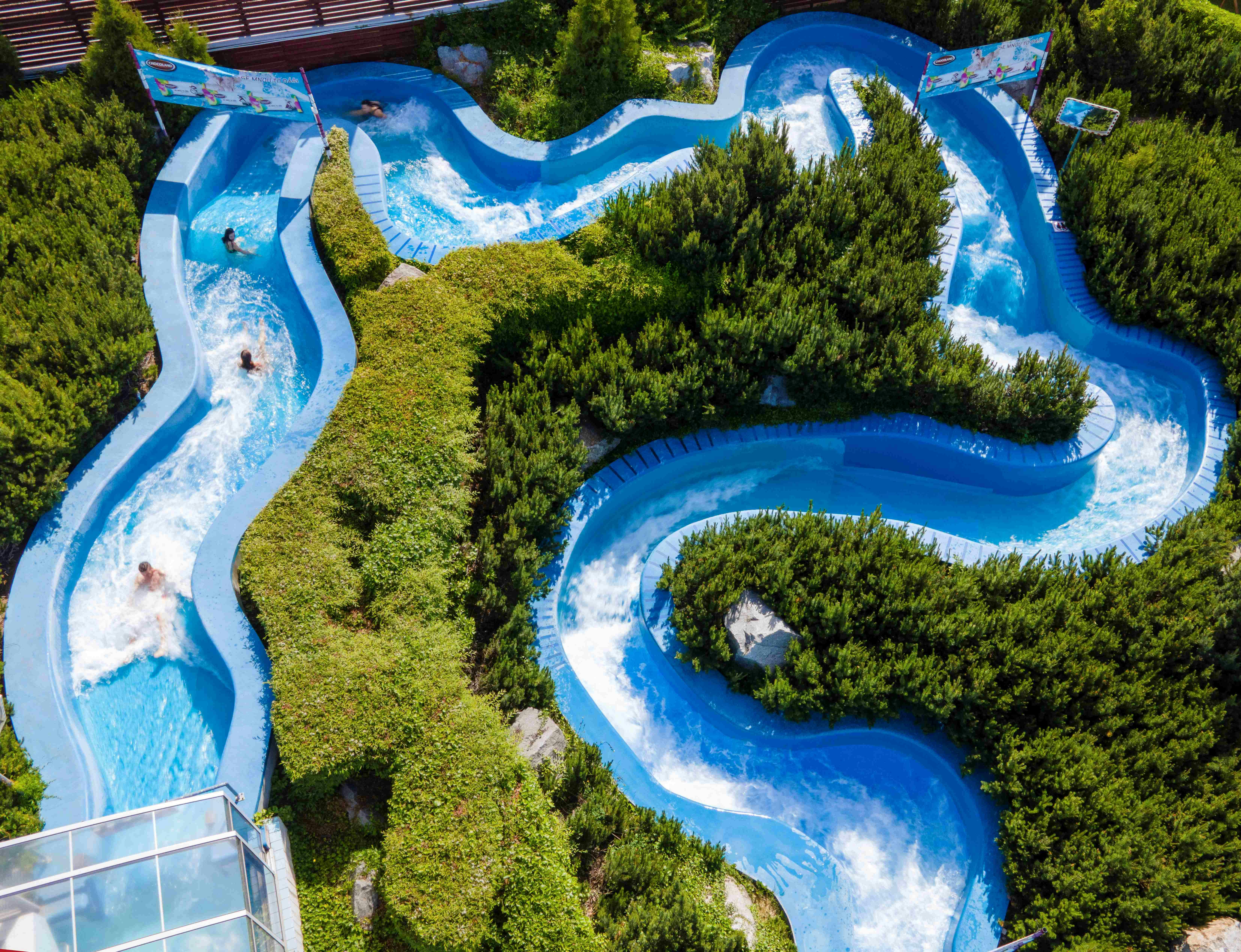 Aerial view of a water park with blue winding slides surrounded by green bushes, where people are enjoying the slides.