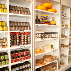 Hyllor fyllda med en mängd olika burkar, flaskor och ostblock i en välorganiserad livsmedelsbutik.