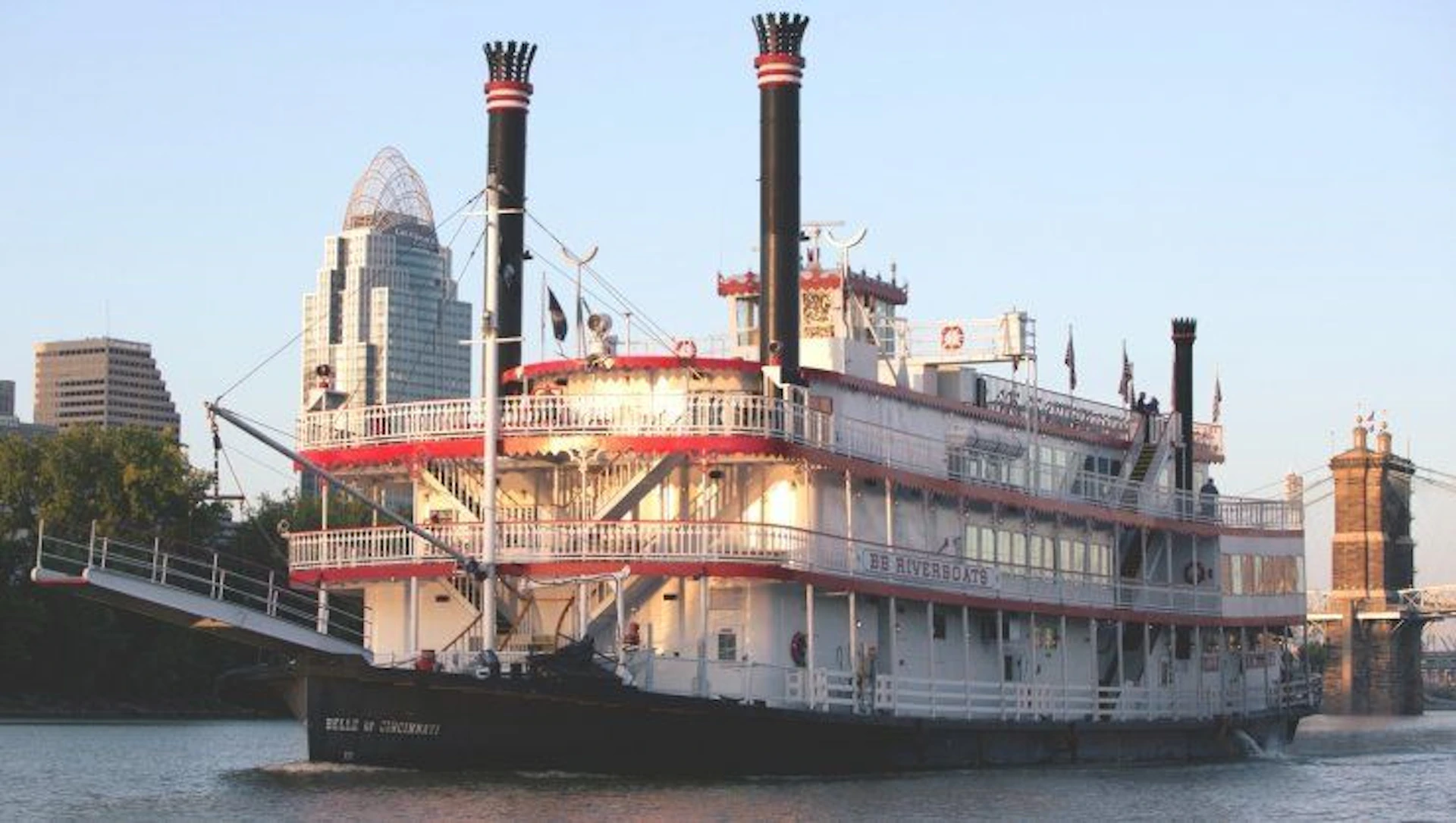 A river steamboat named 'Belle of Cincinnati' docked by a city with tall buildings in the background.