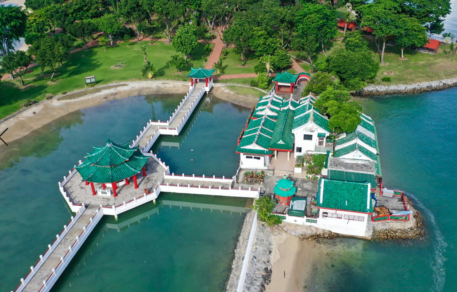 Aerial view of a traditional Chinese-style building and pavilion with green roofs surrounded by water and greenery.