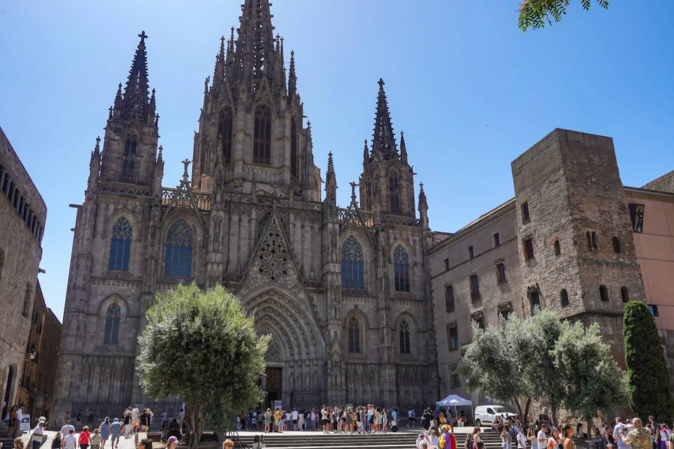 A Gothic-style cathedral with tall spires, a large entrance, and a crowd of people in the foreground under a clear sky.