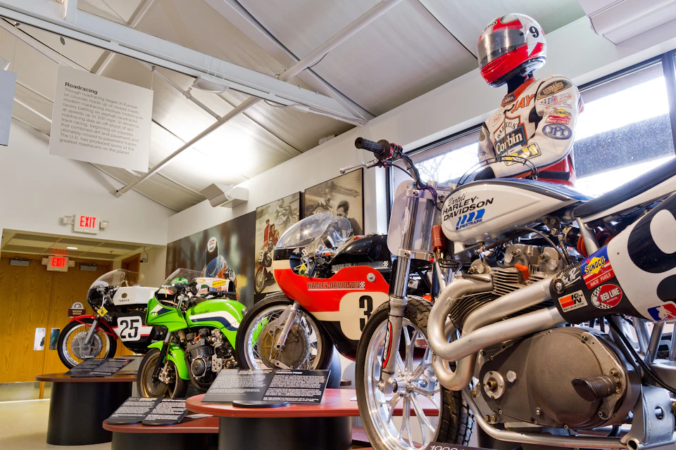 A motorcycle exhibit featuring vintage bikes and a rider mannequin in a racing suit and helmet. Information plaques are visible.