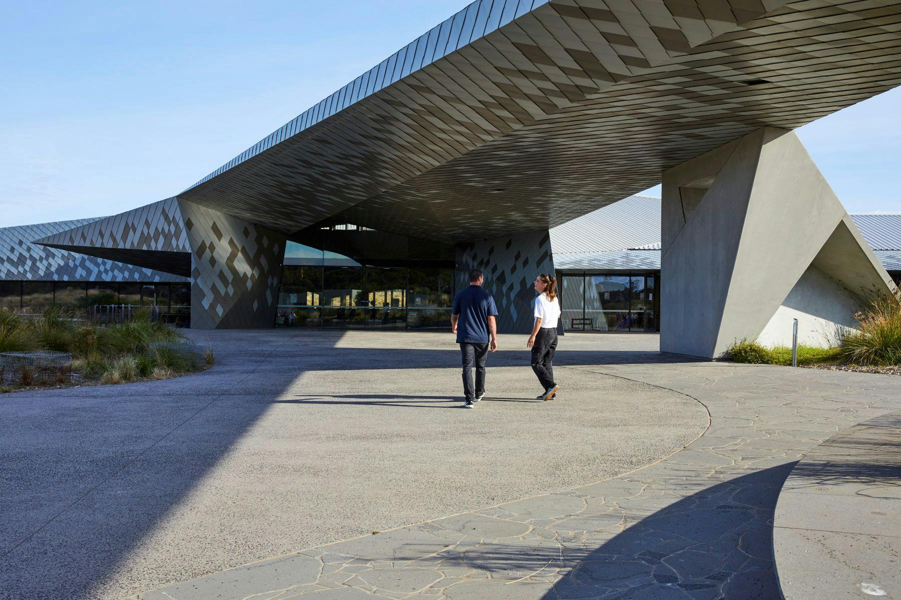 两个人走向一栋现代建筑，在蓝天下有棱角分明的反光建筑。