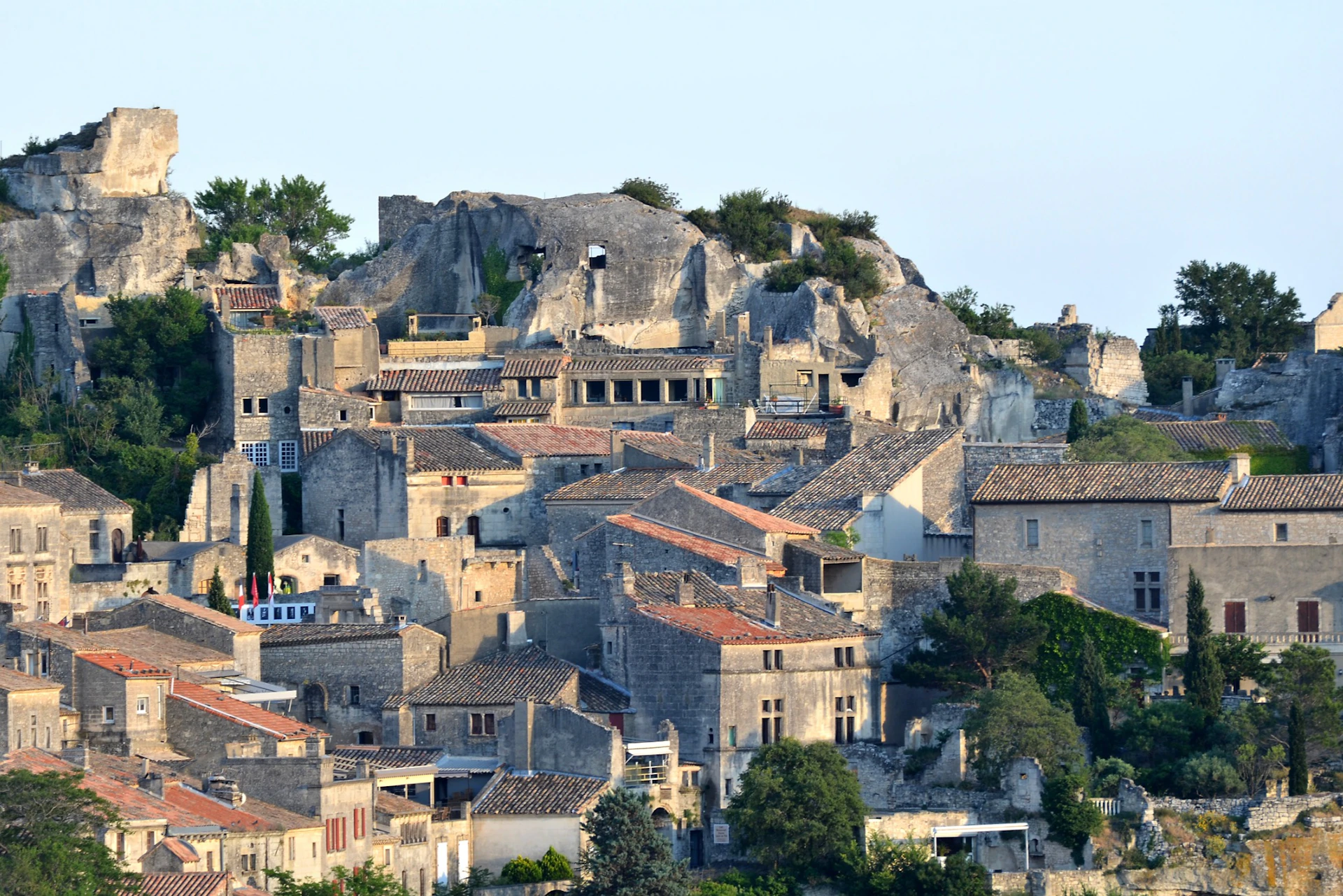 Medieval stone buildings clustered on a hillside with rocky cliffs and greenery in the background.