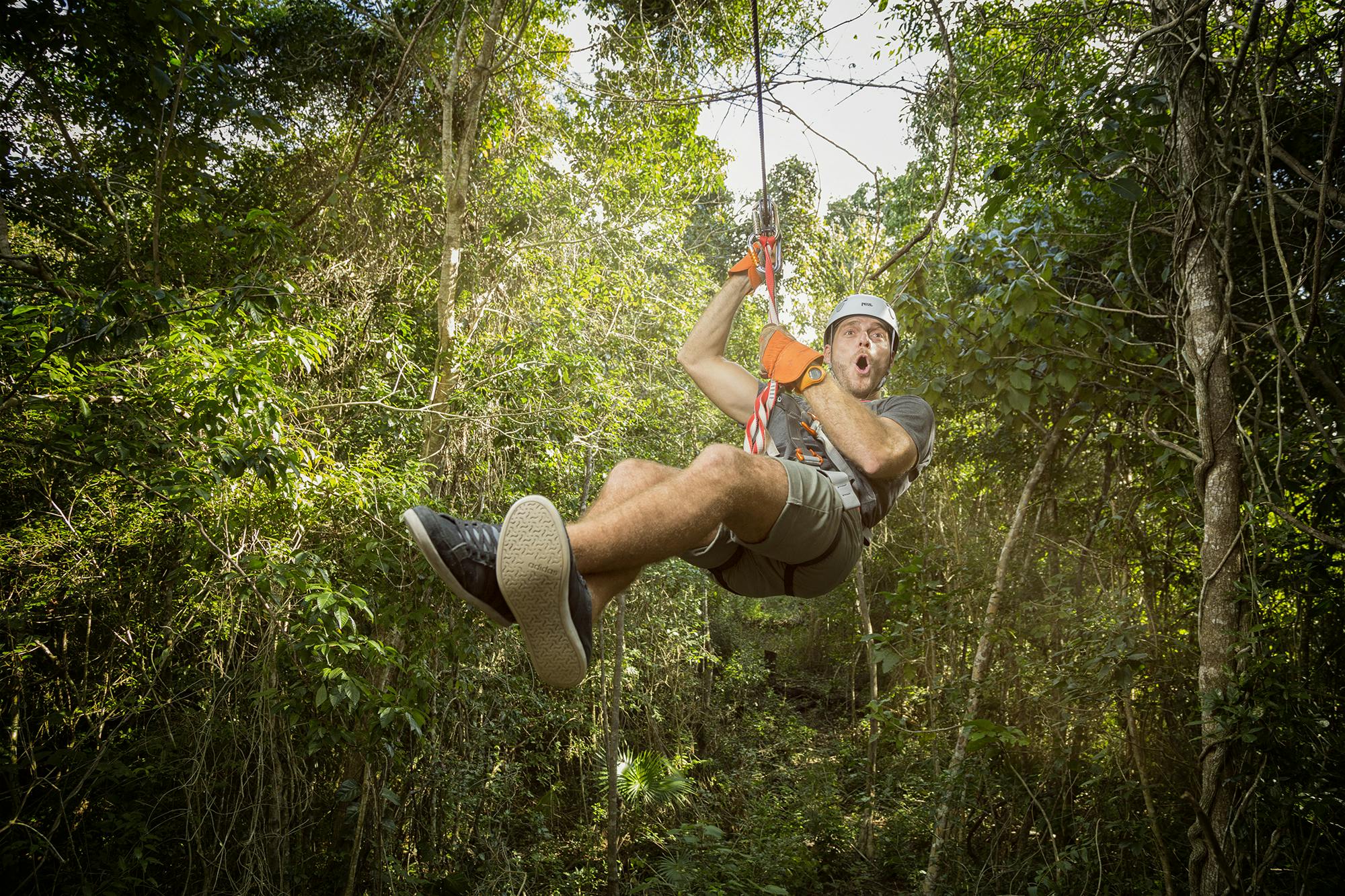 Πρόσωπο με φερμουάρ μέσα από πυκνό δάσος, φορώντας κράνος, γάντια και καθημερινά ρούχα, με μια ενθουσιώδη έκφραση.
