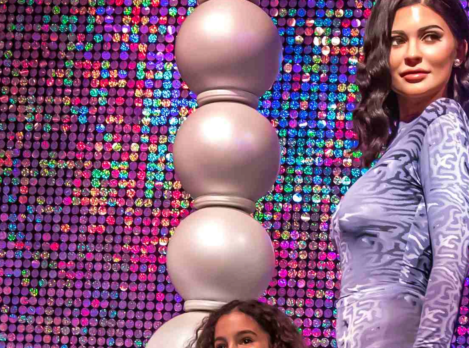 Two adults and two children pose in front of a large, decorative ring with a blue diamond on a glitzy, colorful background.