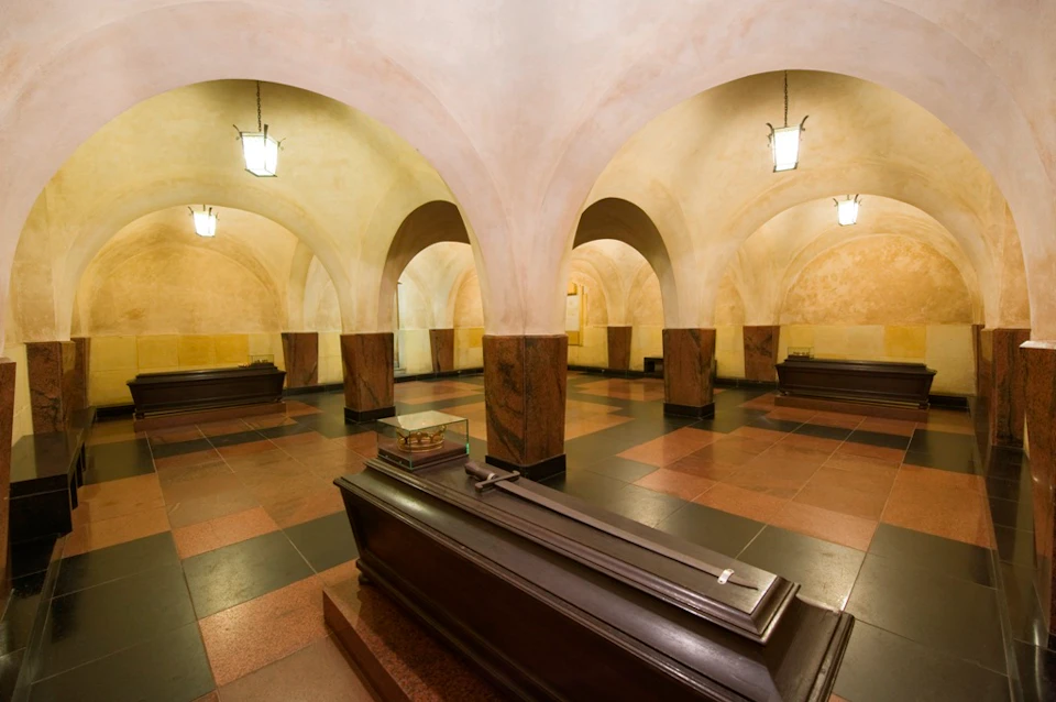 An underground room with arched ceilings, hanging lanterns, and multiple sealed coffins placed on a tiled floor.