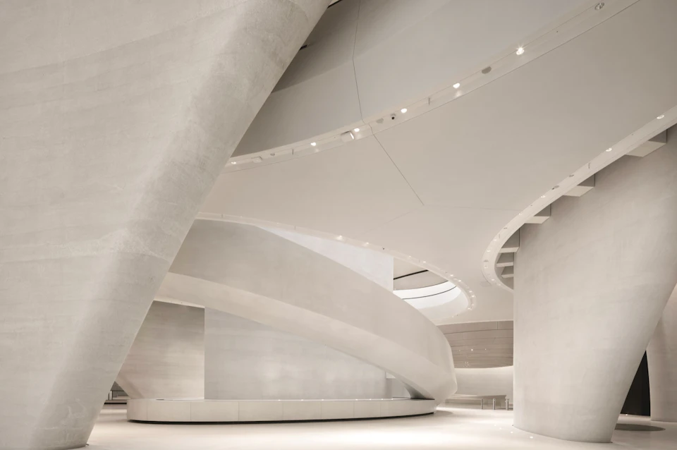 A modern interior featuring curved architectural elements, smooth white surfaces, and soft lighting.