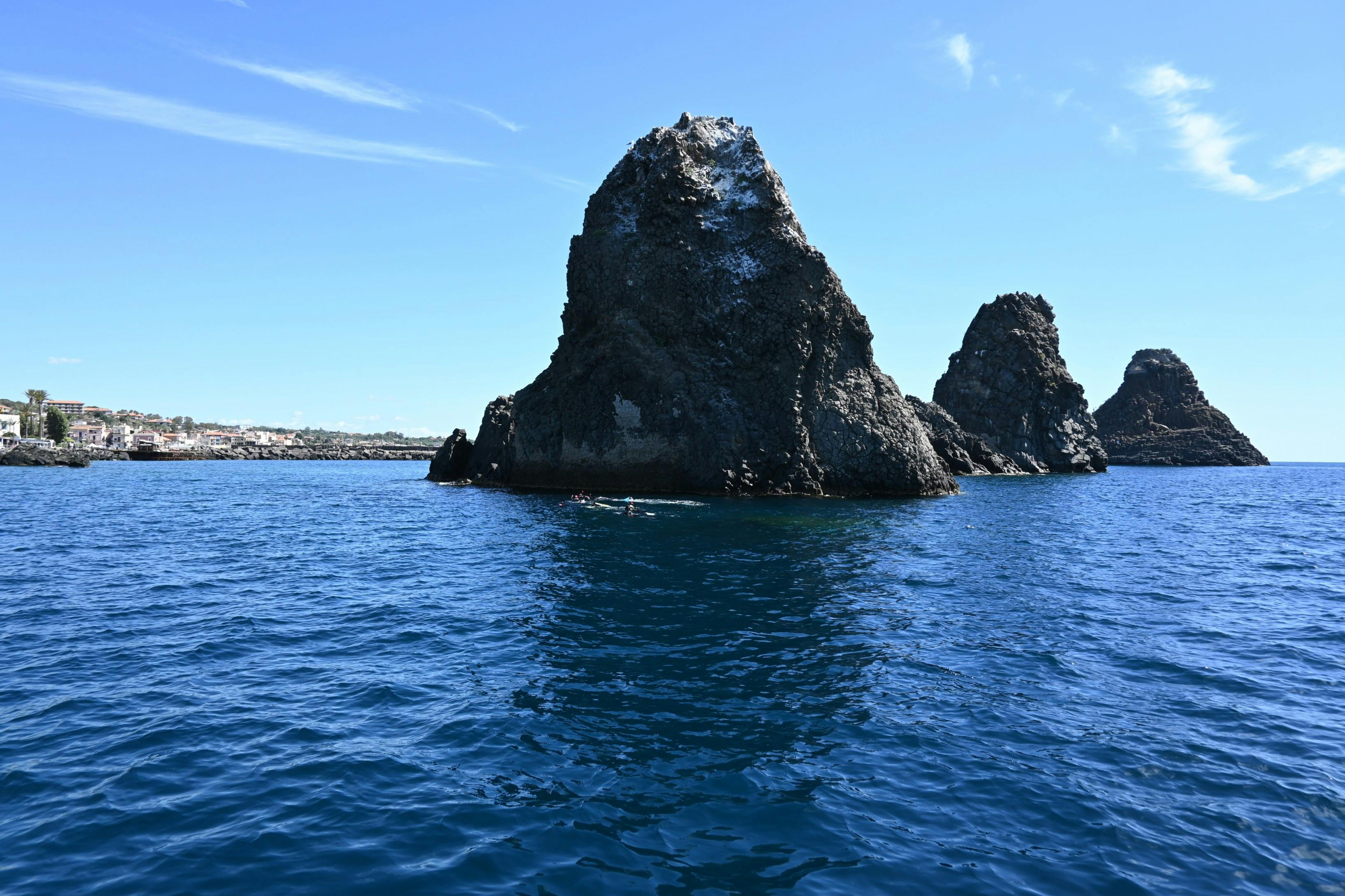 Las formaciones rocosas surgen del profundo mar azul bajo un cielo despejado, con un paisaje urbano lejano visible cerca del horizonte.