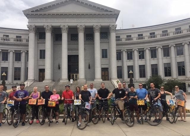 Un groupe de personnes à vélo devant un grand bâtiment de style classique avec des colonnes.