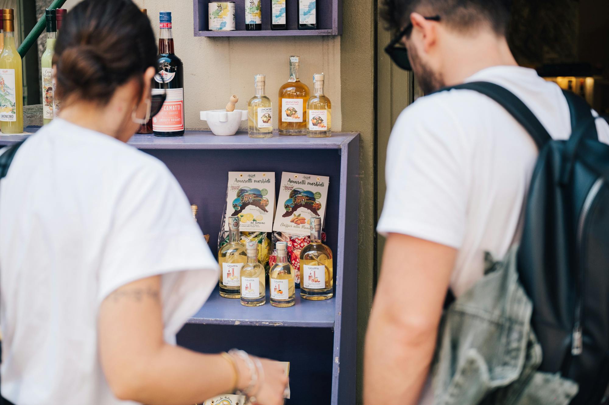 一位背着背包的男士浏览架子，架子上摆放着意大利食品和利口酒的瓶子和包装。