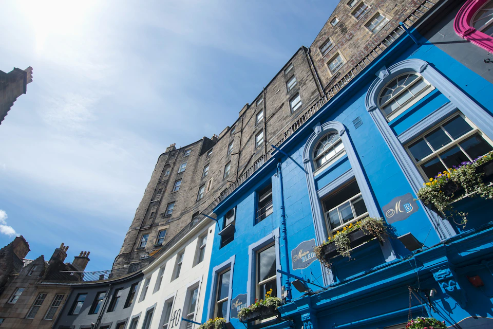 Colorful buildings with blue and white facades under a clear sky, with upper floors of stone buildings visible above.