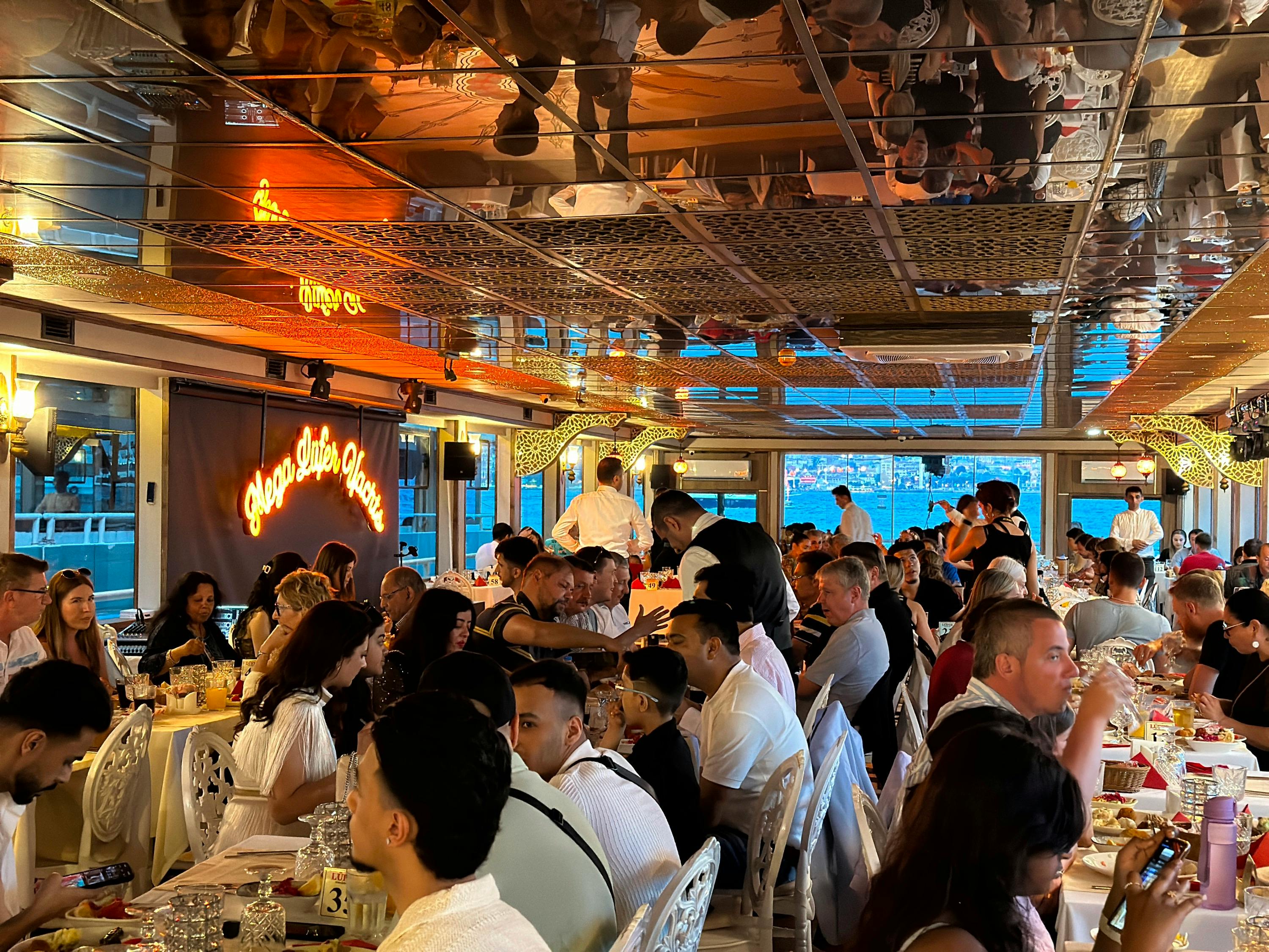 A lively dining scene aboard a boat, with diners at tables, servers attending, and a cityscape visible through windows.
