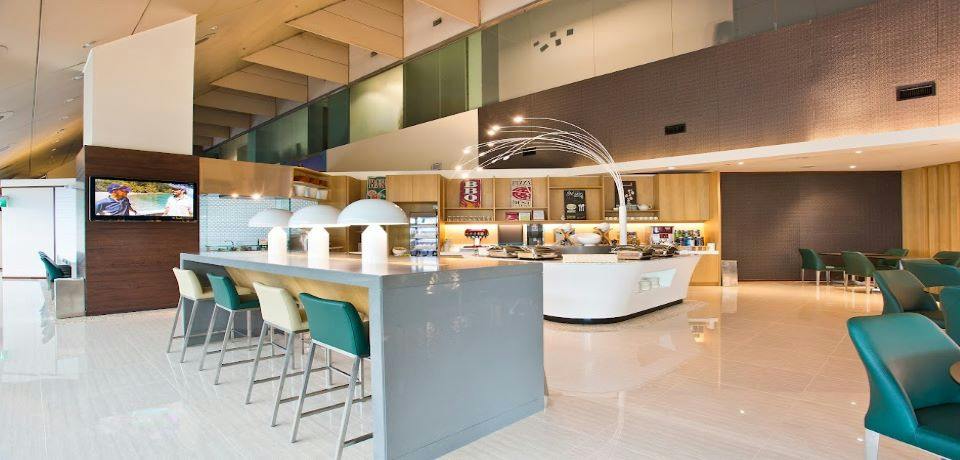 Modern cafe interior with a counter, chairs, decorative lighting, and shelves displaying items in the background.