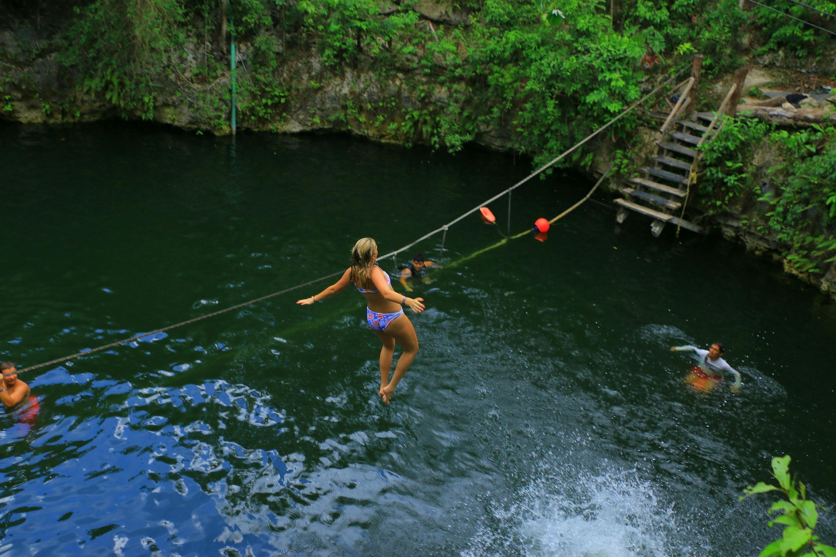 水着姿の人物が、緑と木製の階段を背景にした天然のウォーターホールに飛び込んできました。