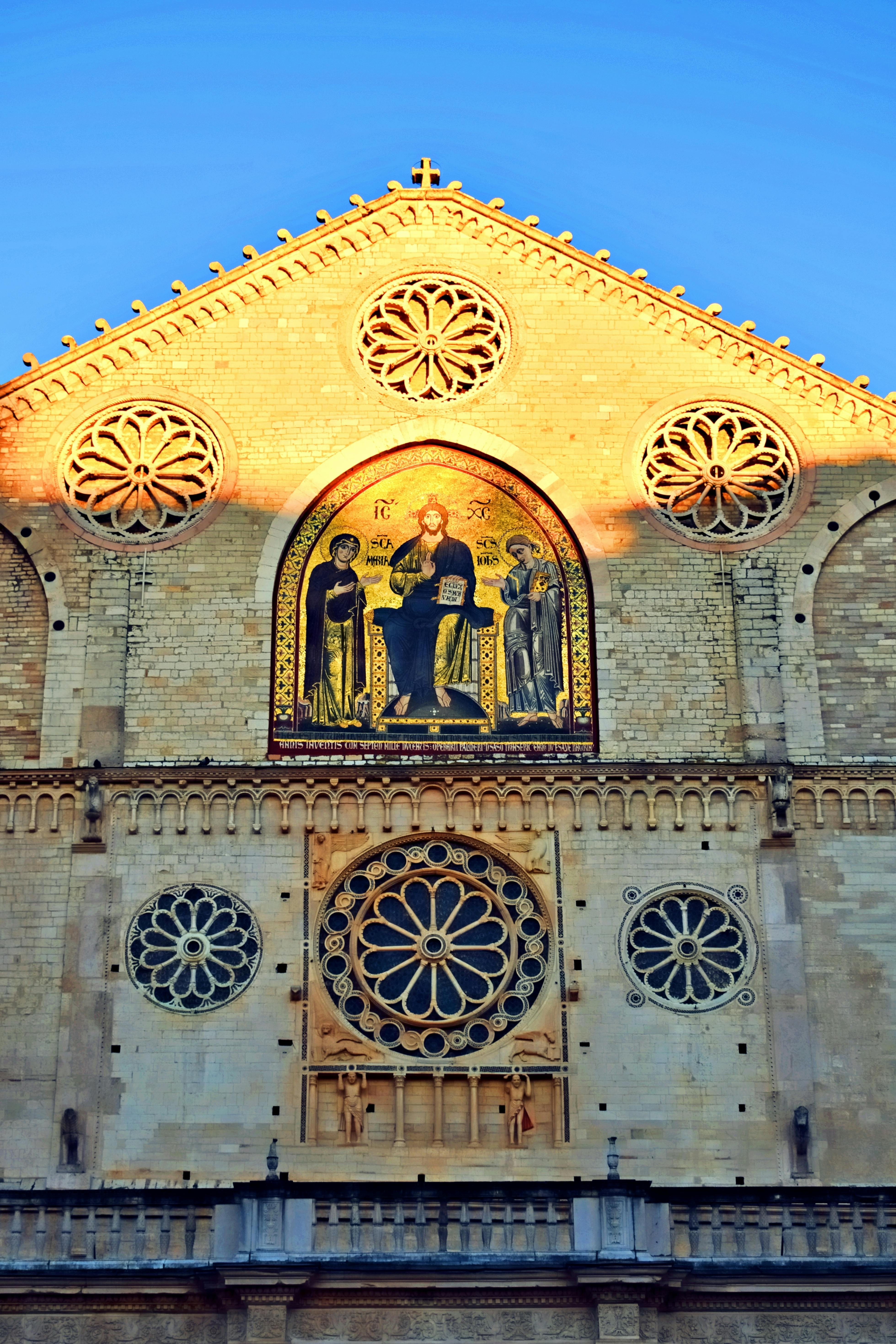 Πρόσοψη πλινθόκτιστου κτιρίου με κυκλικά παράθυρα και ψηφιδωτό που απεικονίζει θρησκευτικές μορφές κάτω από αψίδα.