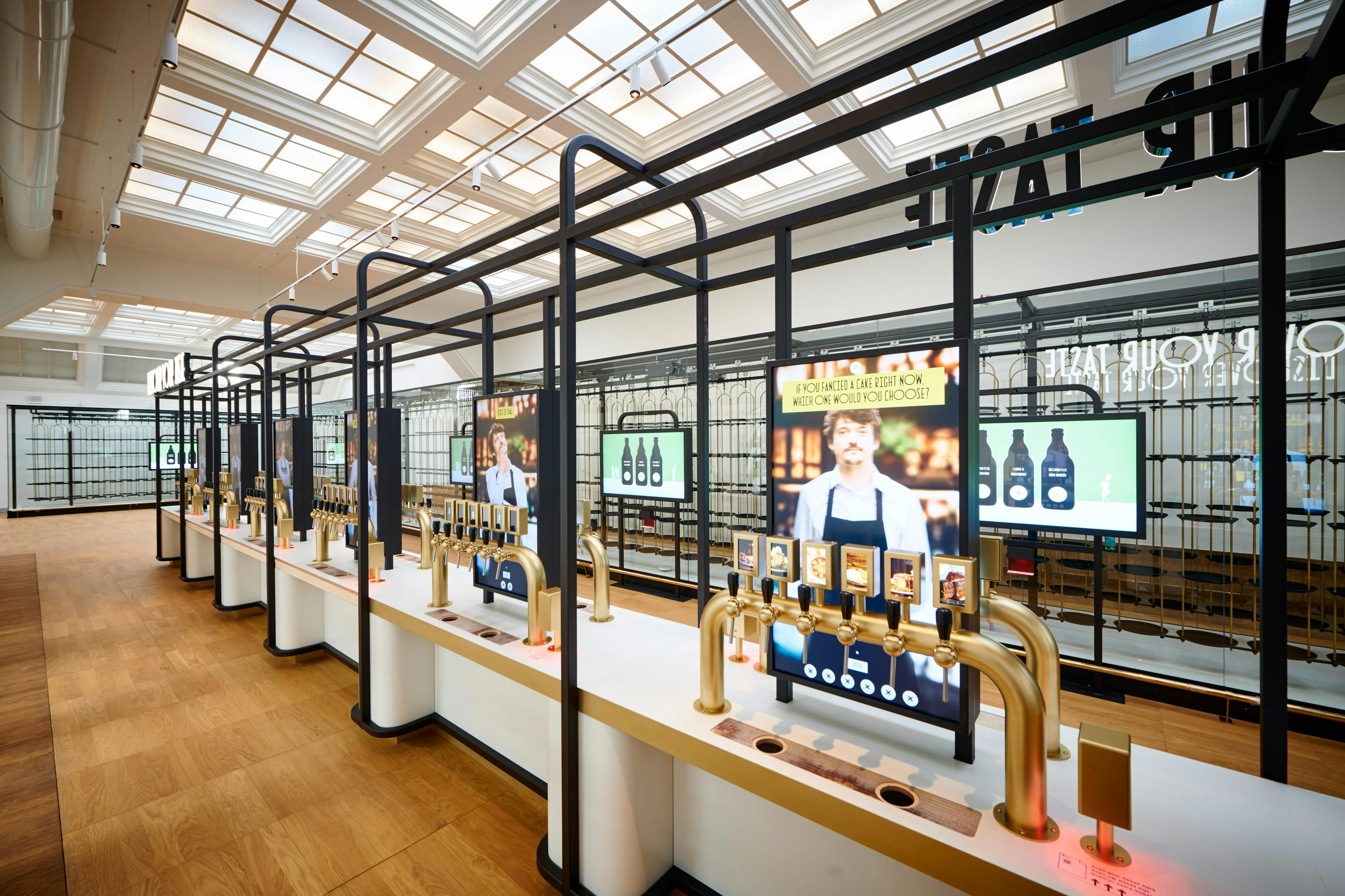 Moderní samoobslužná nápojová stanice s několika mosaznými kohoutky, digitálními obrazovkami a elegantním, prostorným interiérem s dřevěnou podlahou.