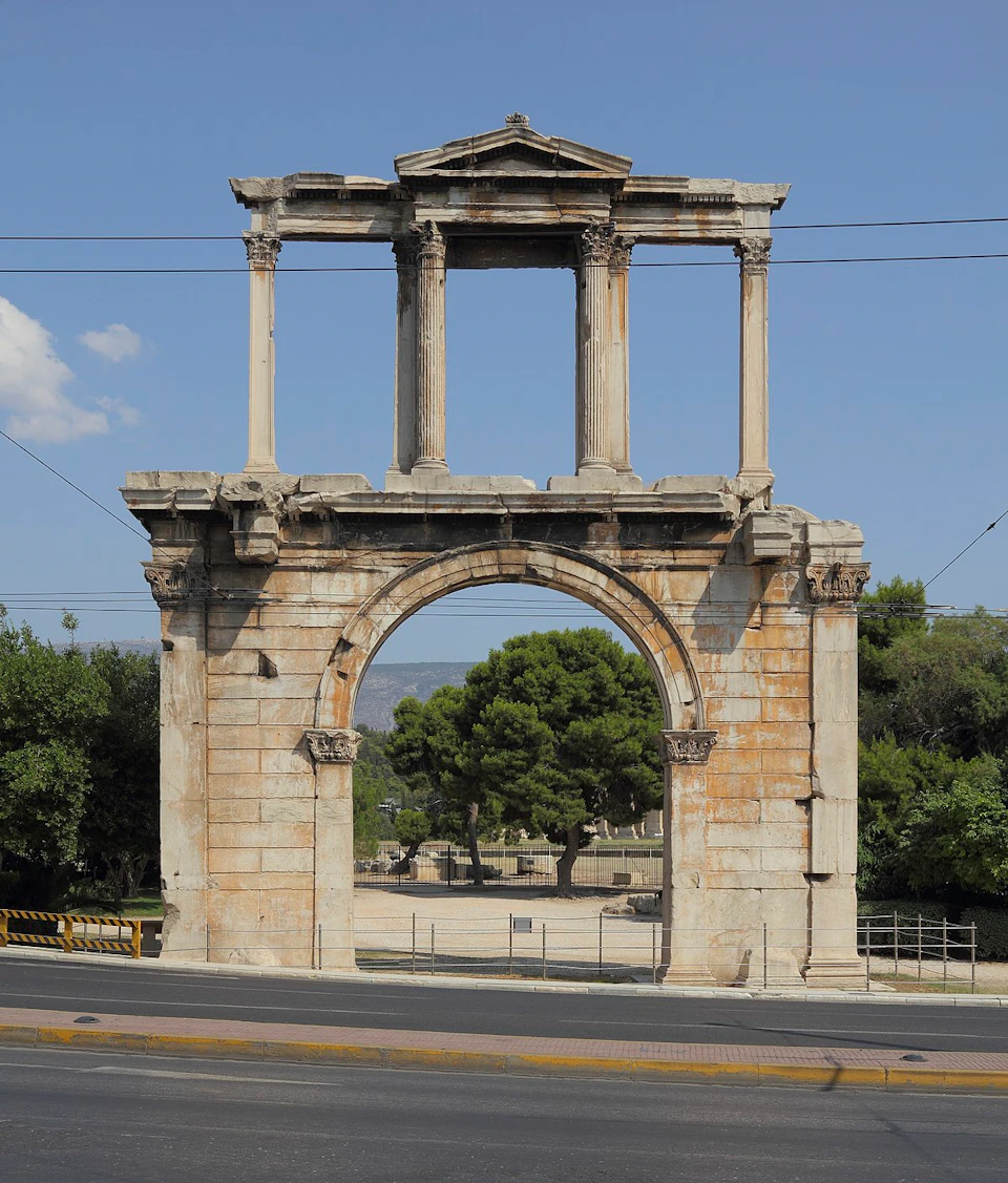 Stone archway standing tall with three columns at the top. Trees and a cloudy sky can be seen in the background.