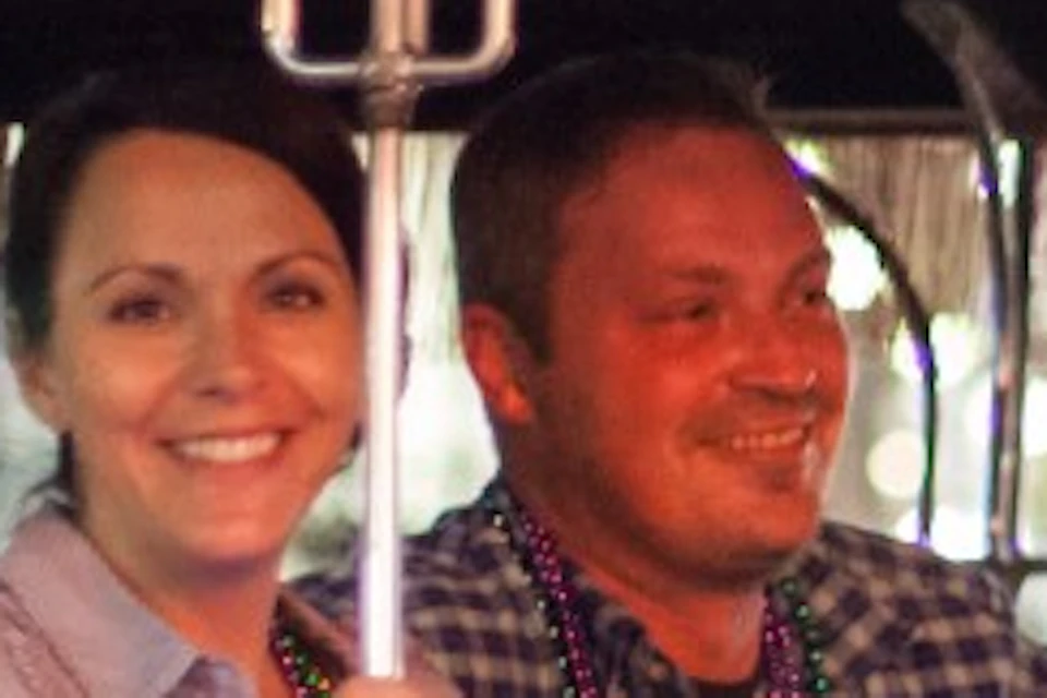 A group of people, smiling and holding drinks, seated on a brightly lit open carriage with “AC 12 943-8820” written on it, at night.