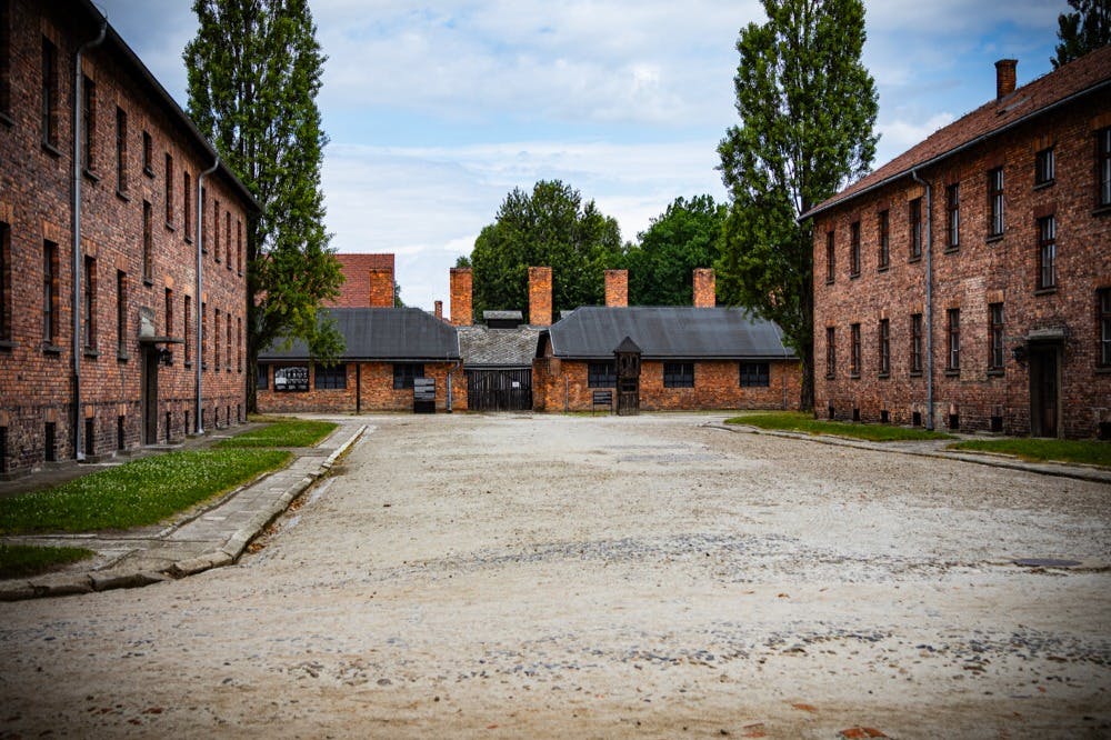 宽敞空荡荡的庭院两侧是红砖建筑，背景是高大的烟囱和绿色植物，笼罩在多云的天空下。