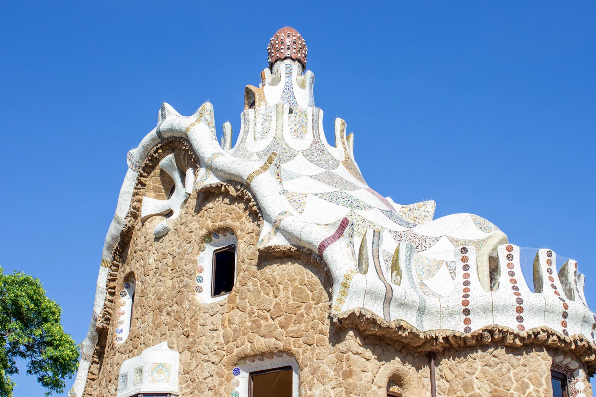A building with a wavy white roof and a textured stone facade under a clear blue sky.