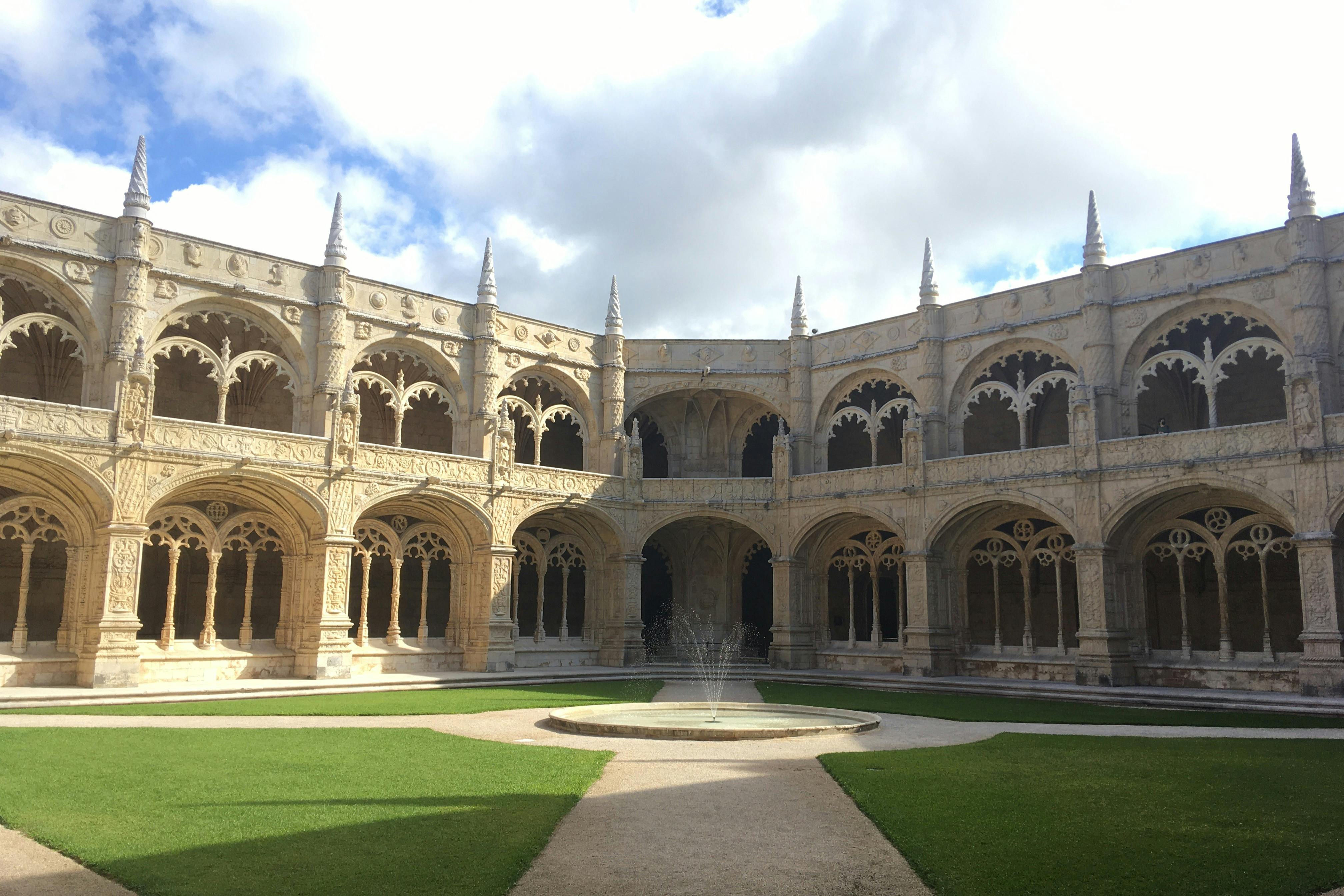 历史悠久的庭院，中心有尖拱门和装饰喷泉，周围环绕着草地和石路。