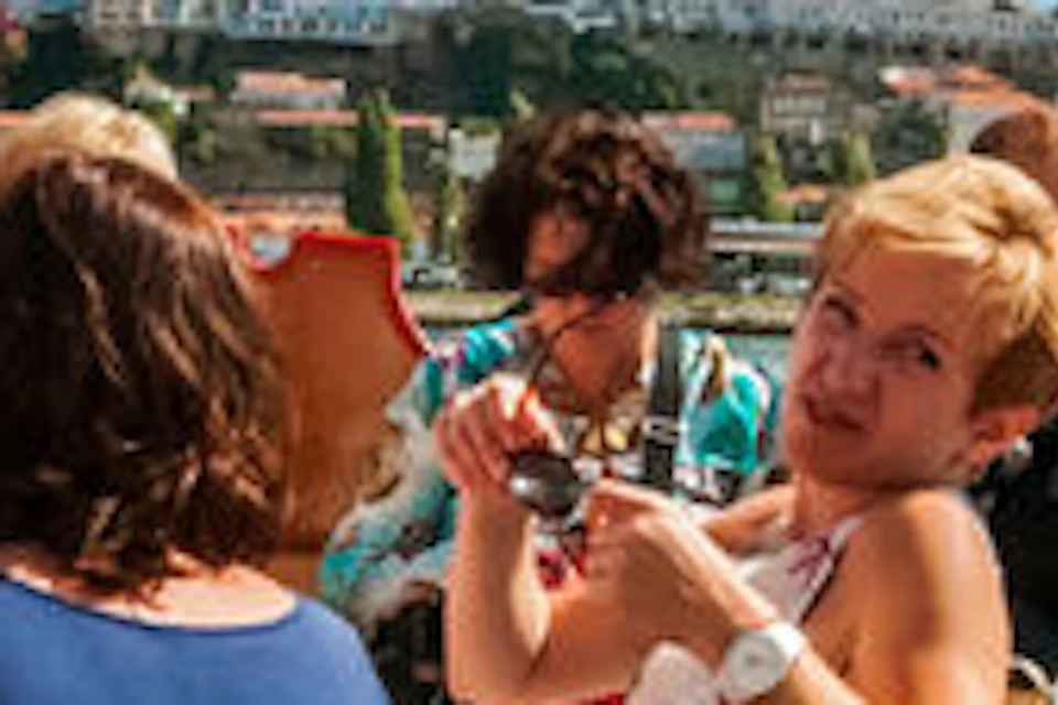 A group of people chatting and enjoying a sunny day on a boat, with a bridge and cityscape visible in the background.