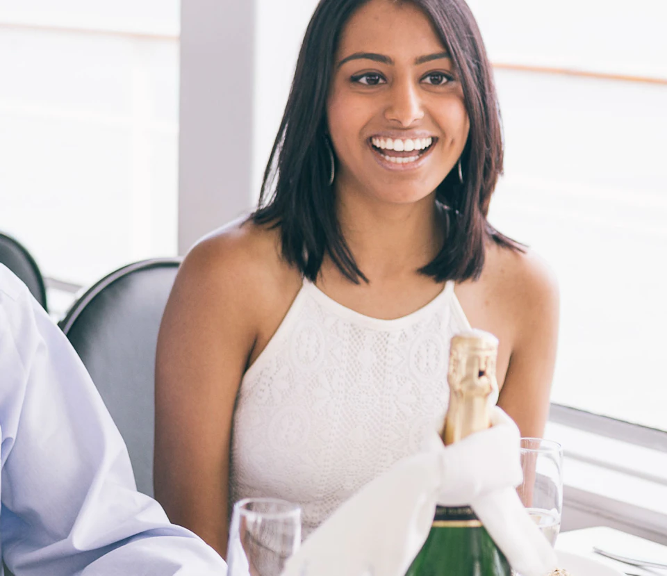 Two people sitting at a table, smiling and enjoying a meal with drinks, in a bright room with large windows.