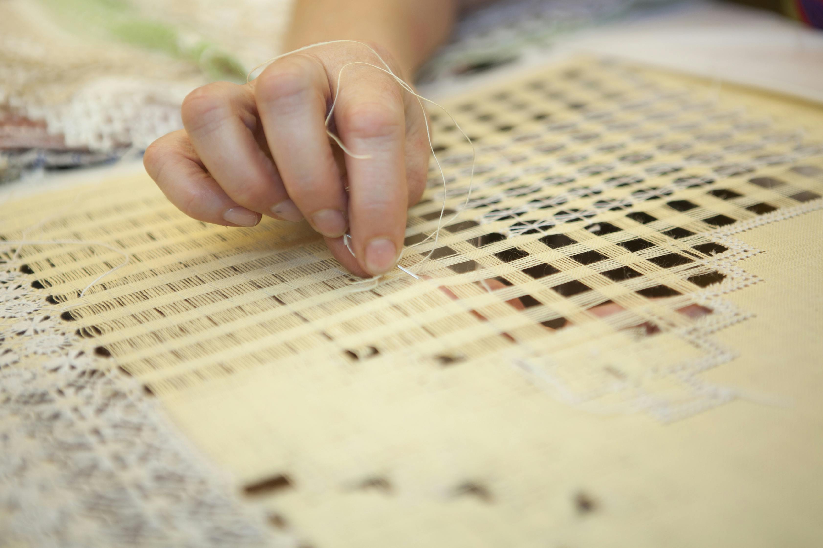 회백색의 격자 무늬 패브릭을 통해 얇은 실을 손으로 짜는 클로즈업.