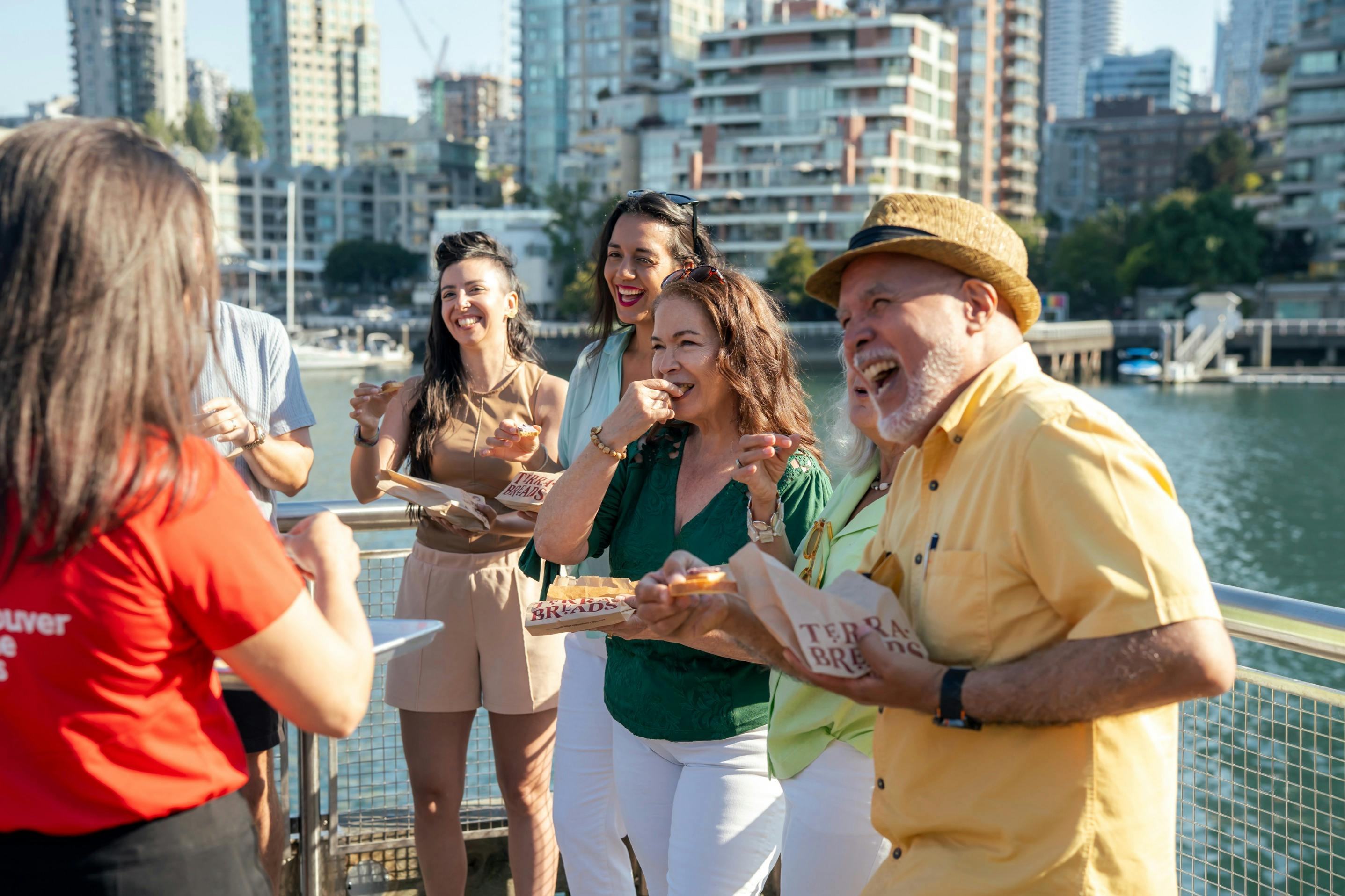 한 무리의 사람들이 건물과 나무를 배경으로 야외에서 미소를 짓고 식사를 하고 있습니다.