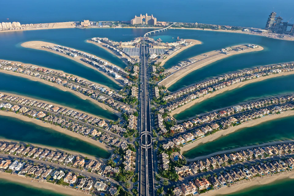 Aerial view of a palm-shaped artificial island with residential areas and a large resort at the top, surrounded by the sea.