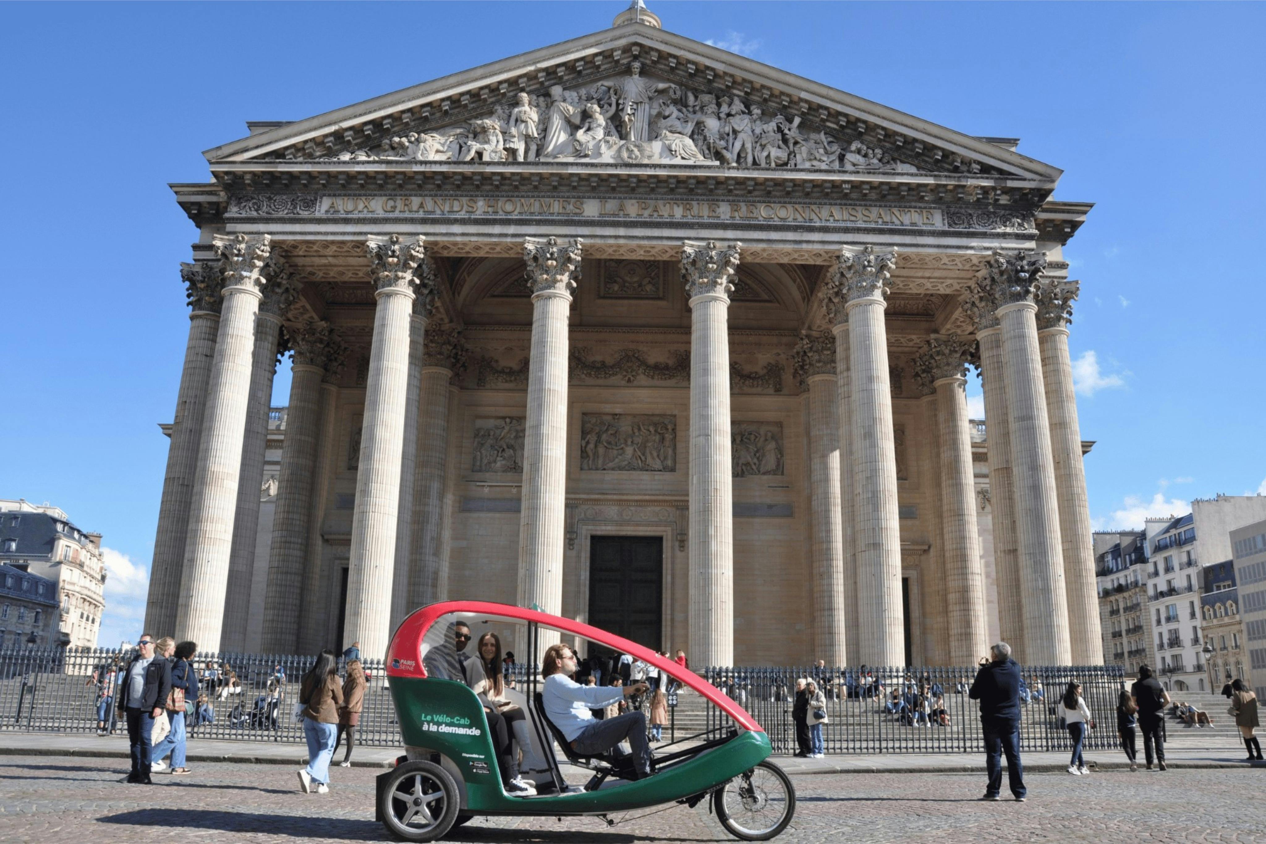 A man drives a green and red pedicab in front of a large neoclassical building with tall columns under a clear blue sky.