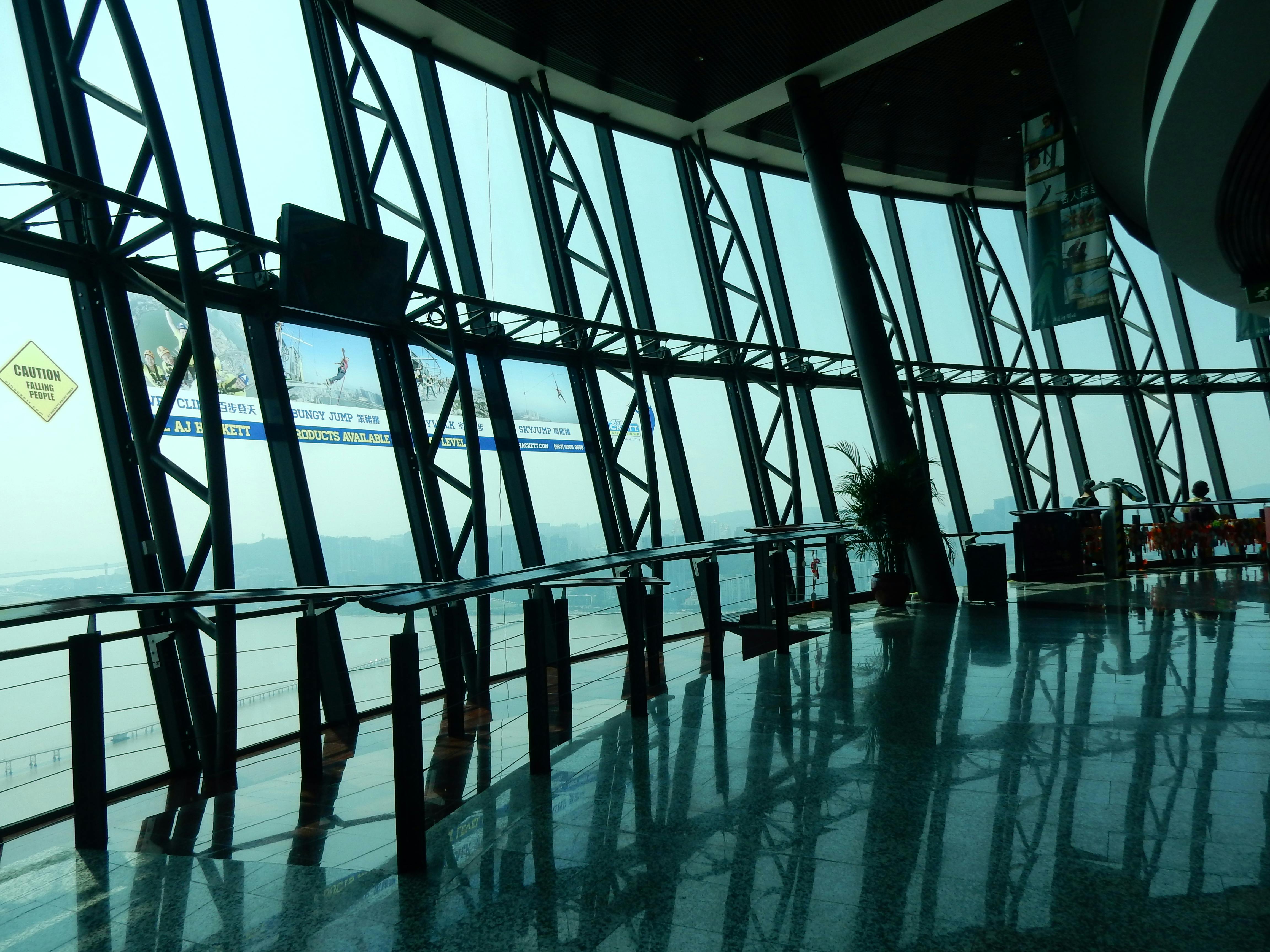Interno di un moderno edificio con pareti di vetro, grandi finestre, travi metalliche e pavimento riflettente. Sono visibili alcune piante in vaso.