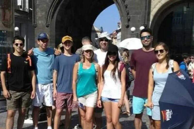 天気のいい日に、石のアーチの前に立って微笑む人々のグループ。 傘を持って夏服を着る人もいます。