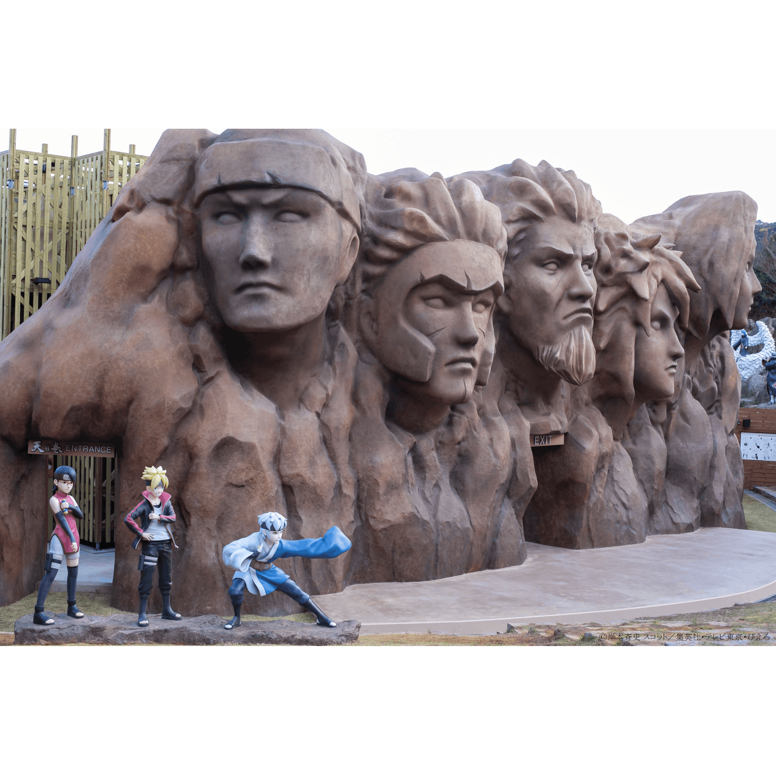Four life-sized statues of anime characters in front of a rock formation with five carved faces.