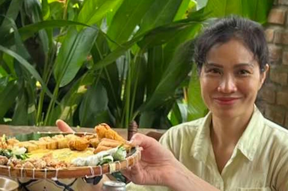 Three people sit at a table outside, enjoying a variety of food and drinks, surrounded by lush greenery.
