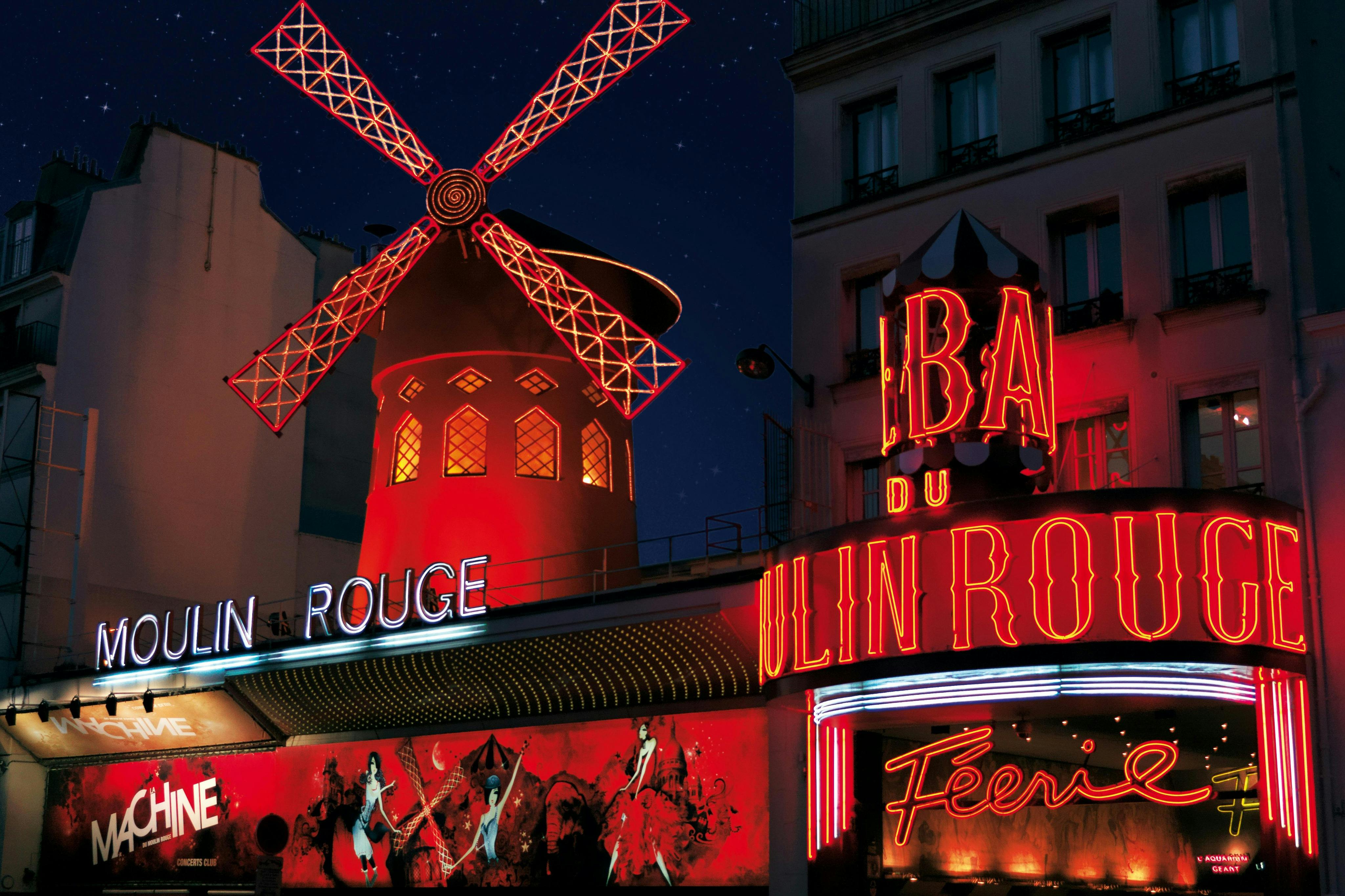 Vista nocturna del Moulin Rouge amb el seu emblemàtic molí de vent vermell i llums de neó brillants.
