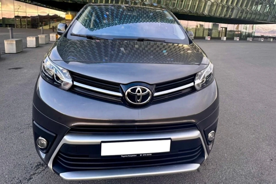 Front view of a parked Toyota car with a showroom in the background, reflecting on the windshield and hood.