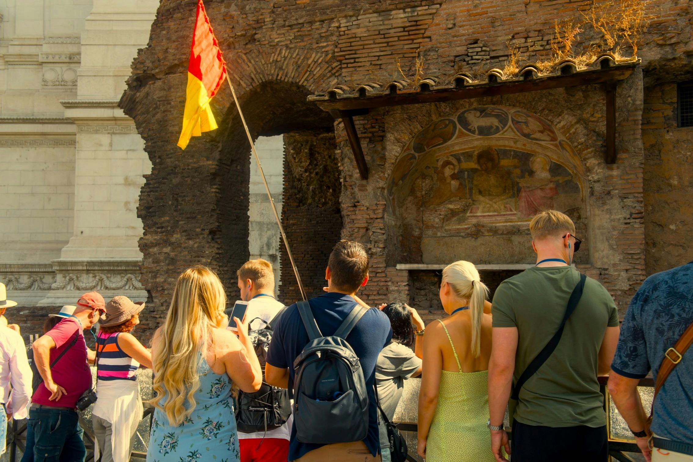Un gruppo di turisti in piedi vicino a un'antica struttura in mattoni, con uno che tiene una bandiera rossa e gialla su un'asta.