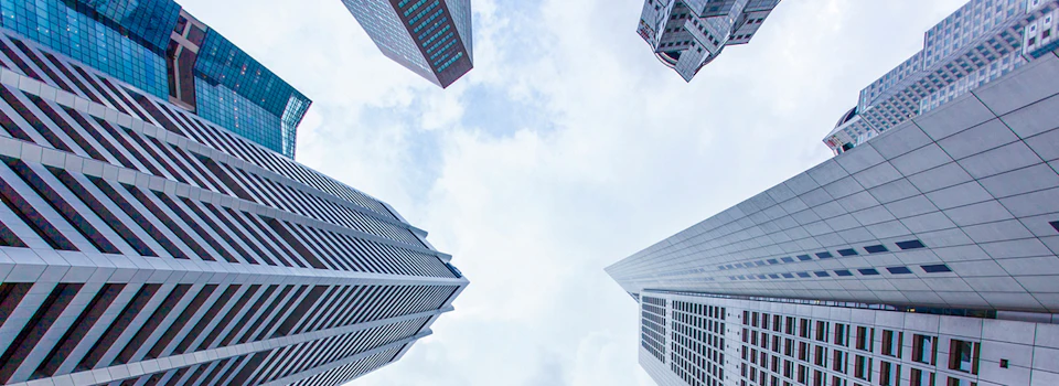 Looking up at four tall skyscrapers from below, set against a partly cloudy sky.