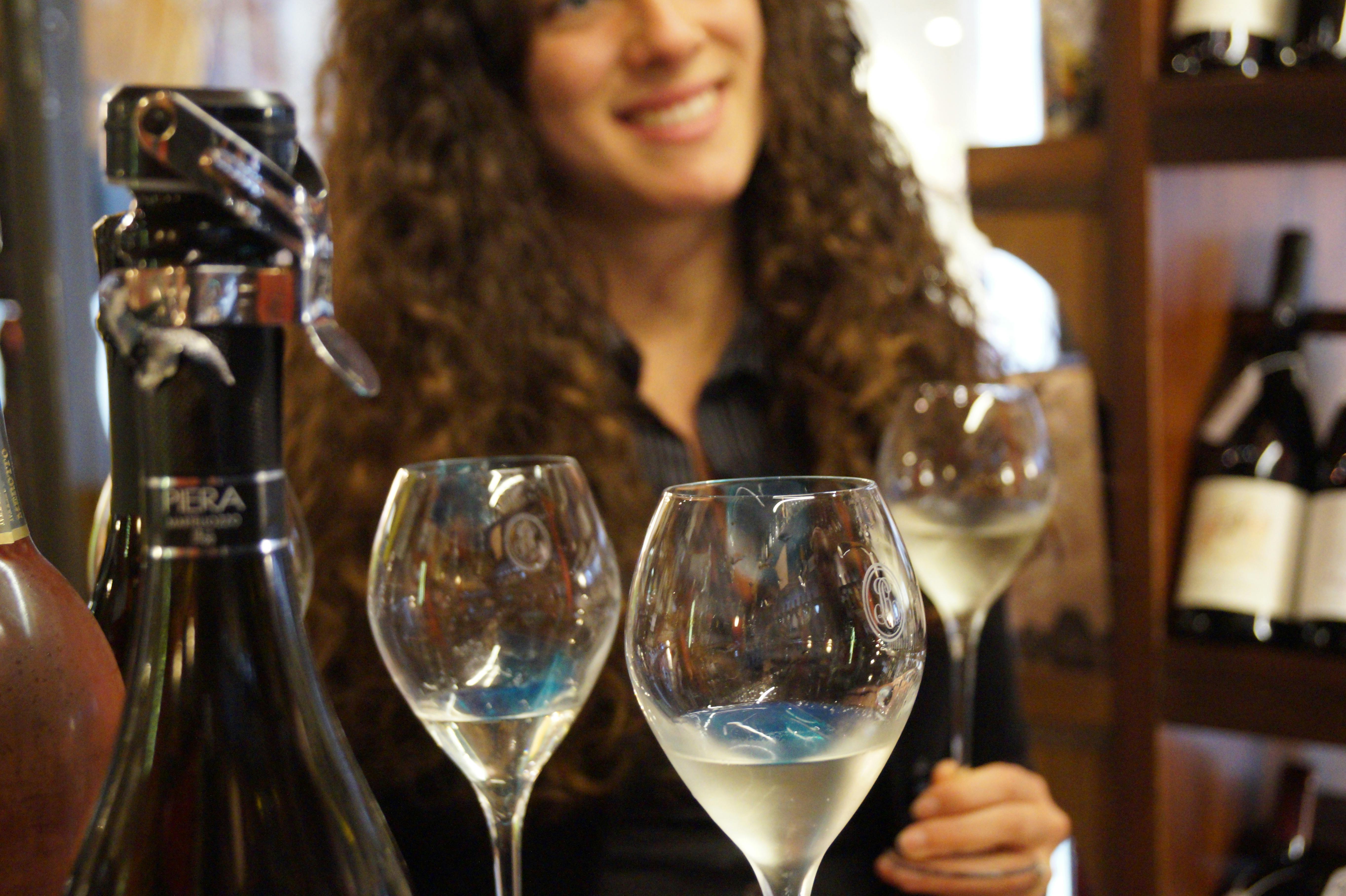 一个人在背景中微笑，前景是一个瓶子和三个装满白葡萄酒的酒杯。