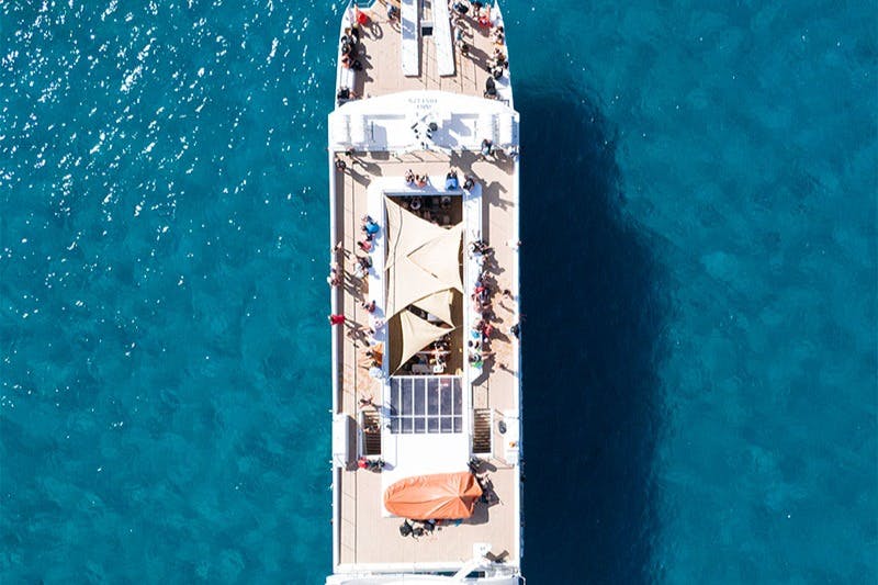 Εναέρια άποψη πολυσύχναστης βάρκας με σκίαστρο και καθιστικό, περιτριγυρισμένη από καταγάλανα νερά.