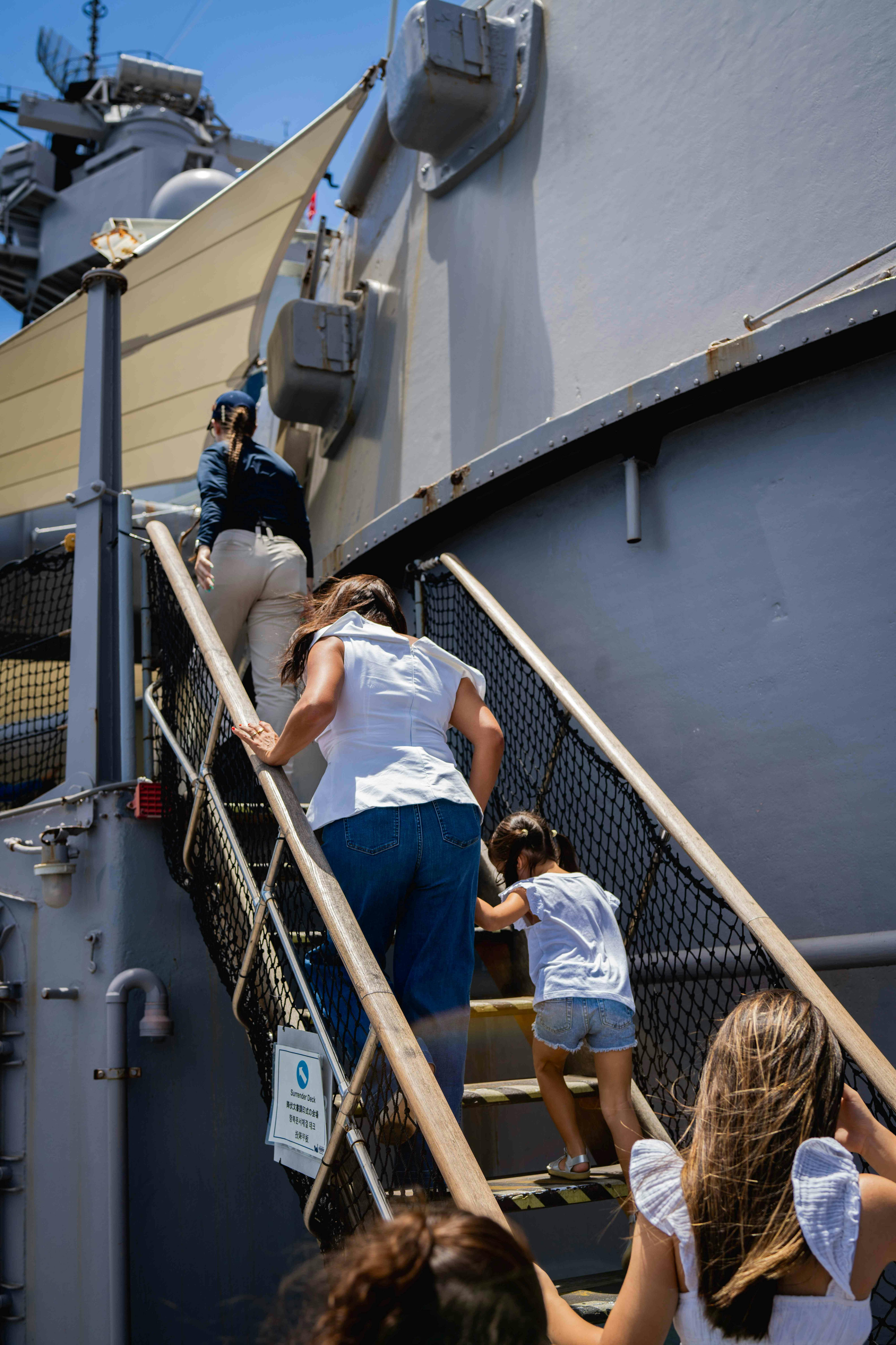 Una donna e un bambino salgono una serie di scale su una nave, seguendo un'altra persona. Lo sfondo mostra l'esterno della nave.