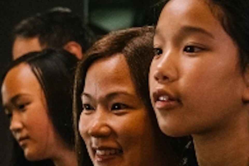 Three people, including two young girls, are closely examining a display in a museum with green metal arches in the background.