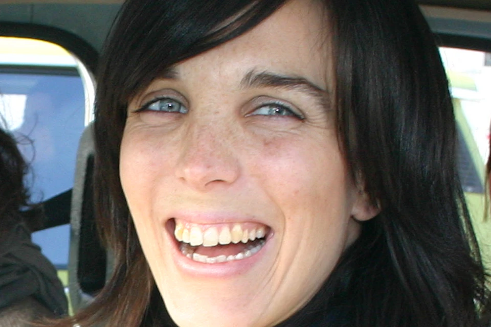 Three smiling women are seated inside a car, with one woman in the driver’s seat and the others in the back.