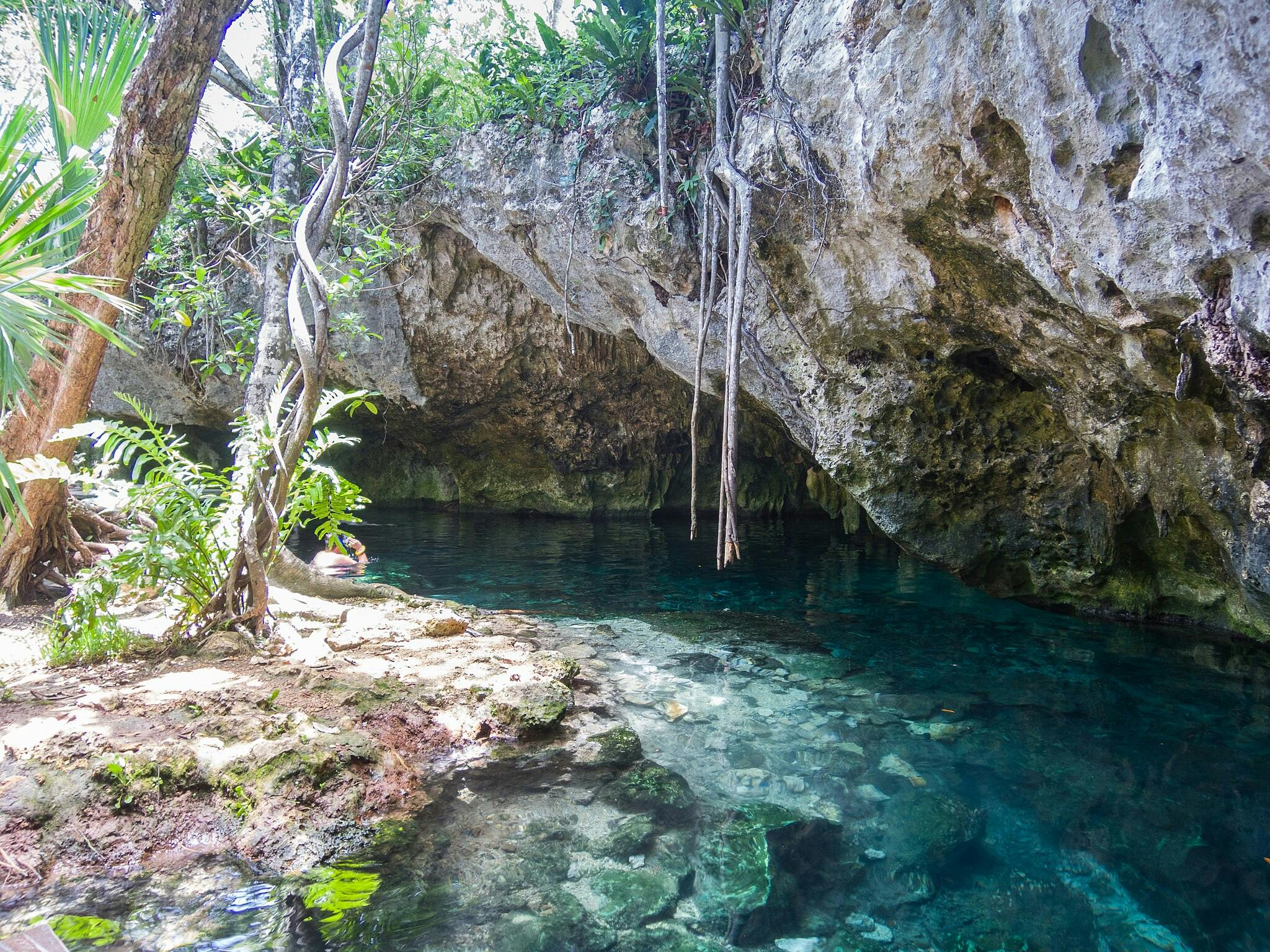 Laguna di acqua limpida circondata da sporgenze rocciose e vegetazione lussureggiante, con una persona che indossa l'attrezzatura per lo snorkeling vicino all'acqua.