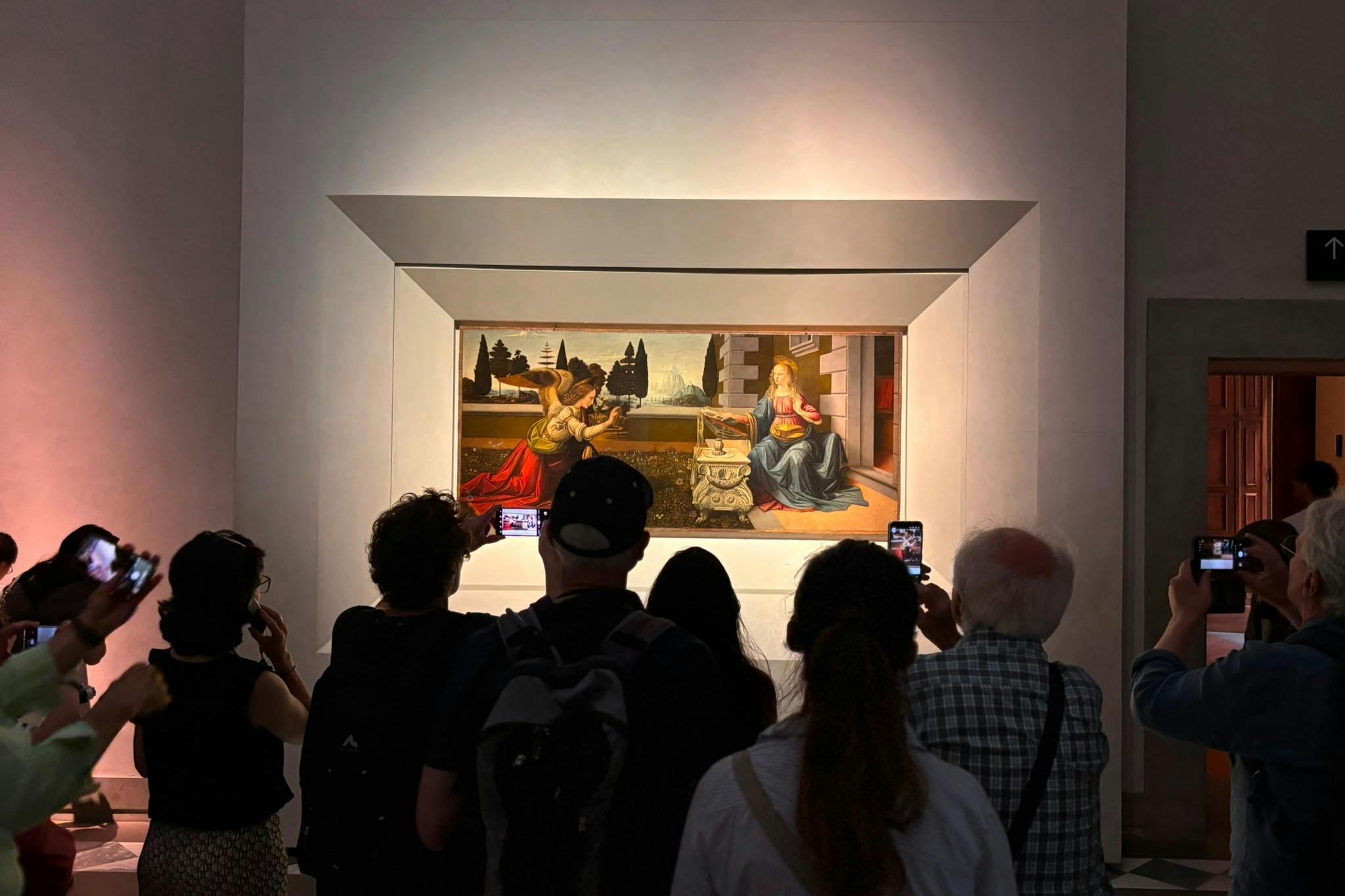 Pessoas em frente a um quadro emoldurado, exposto numa galeria de um museu, a tirar fotografias e a observar a obra de arte.
