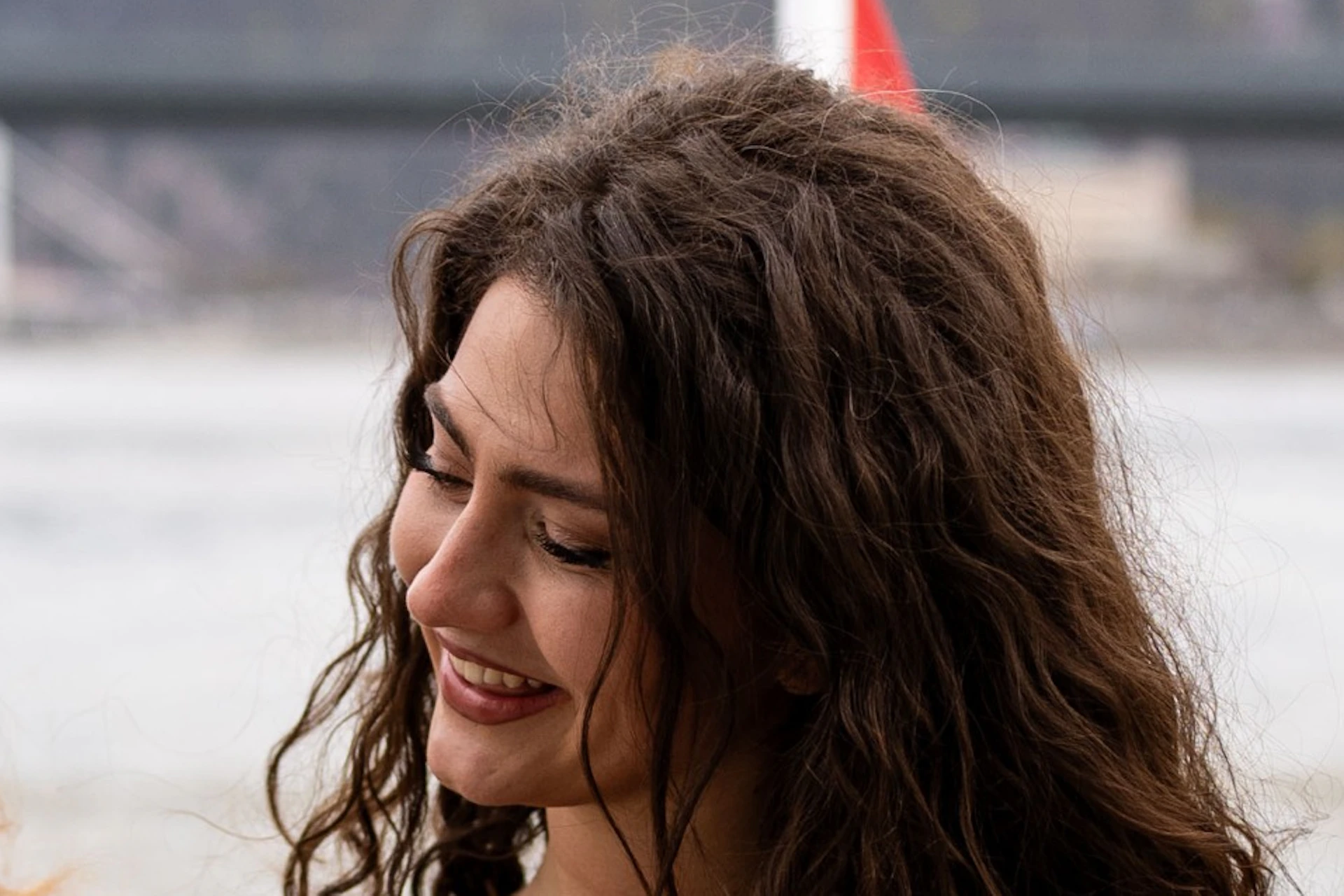 Two women smiling, holding champagne glasses on a boat, with a bridge and river in the background.
