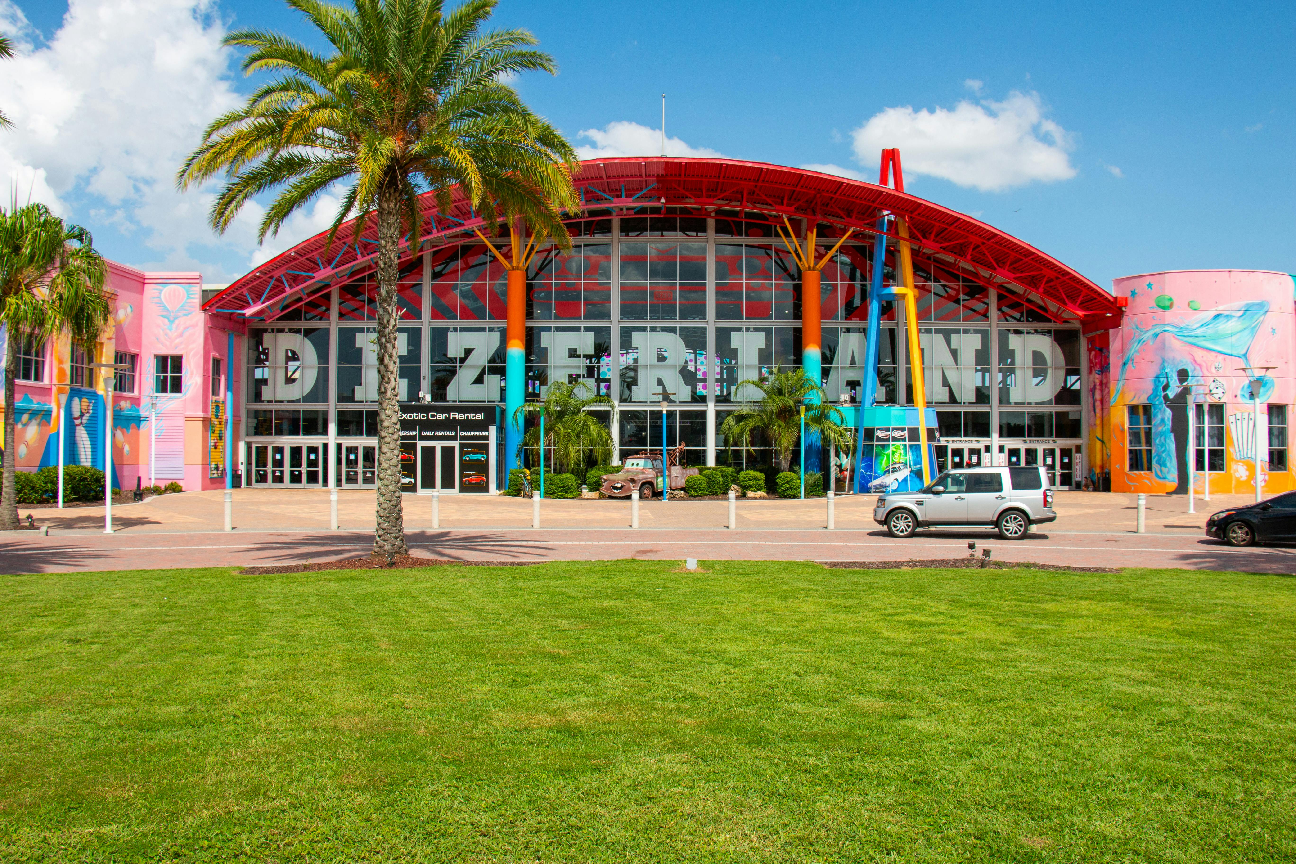Colorful building facade with the large word "DEZERLAND," flanked by palm trees, cars, and vibrant murals.