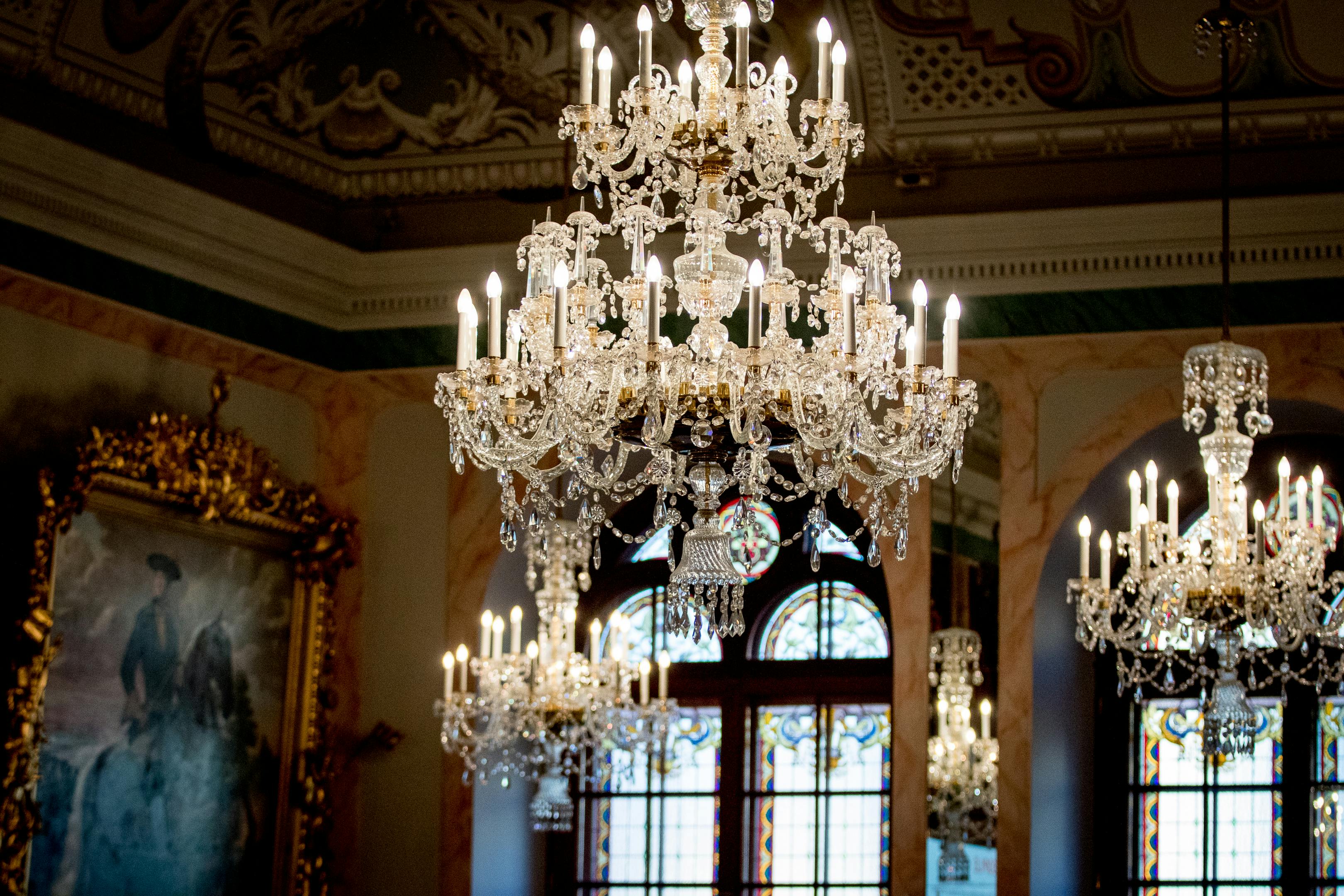 优雅的水晶吊灯和点燃的蜡烛挂在华丽的房间里，窗户是大拱形的，天花板是装饰性的。